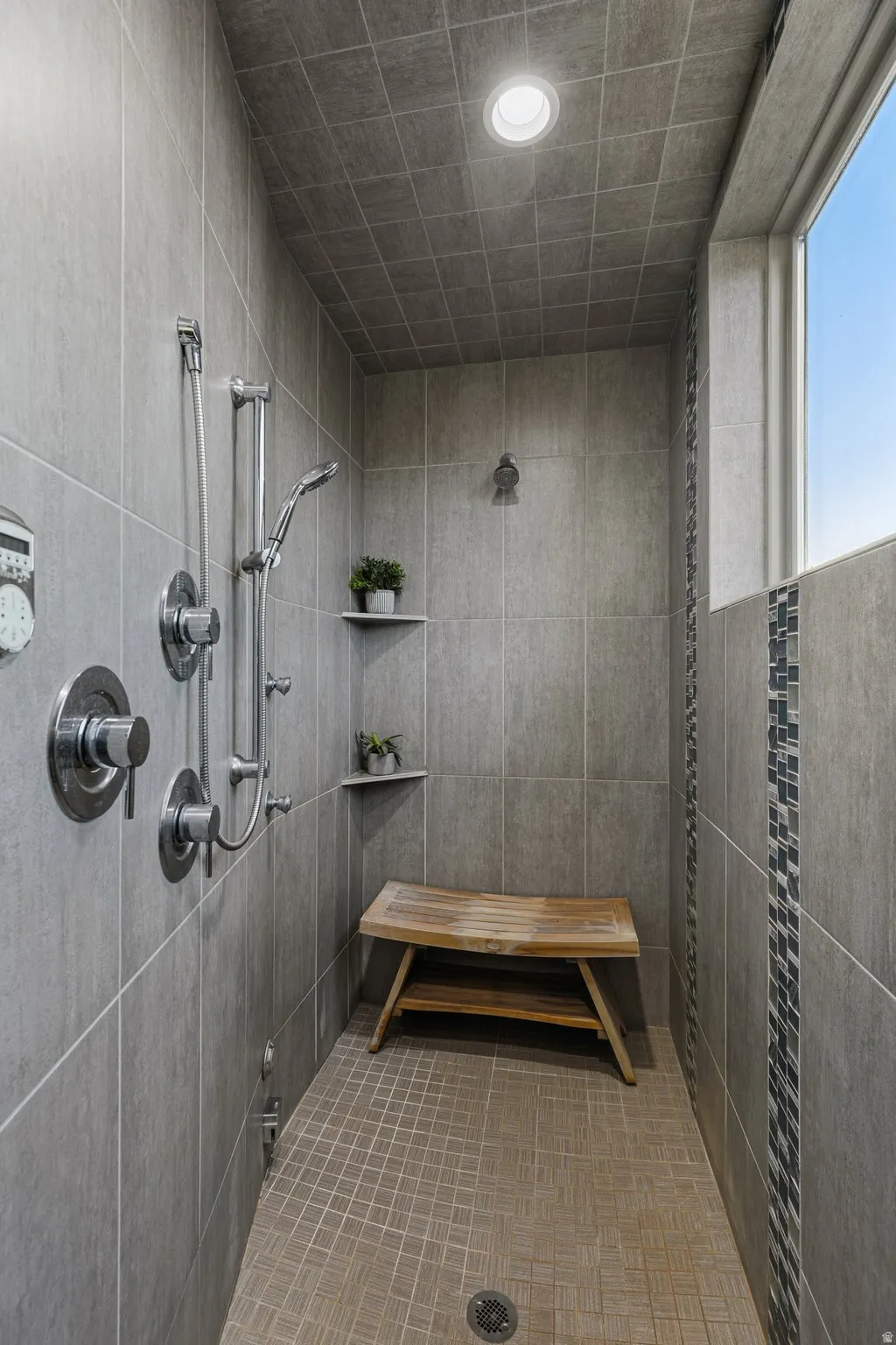 Tiled shower with a built-in bench, corner shelves, multiple showerheads, and a horizontal window