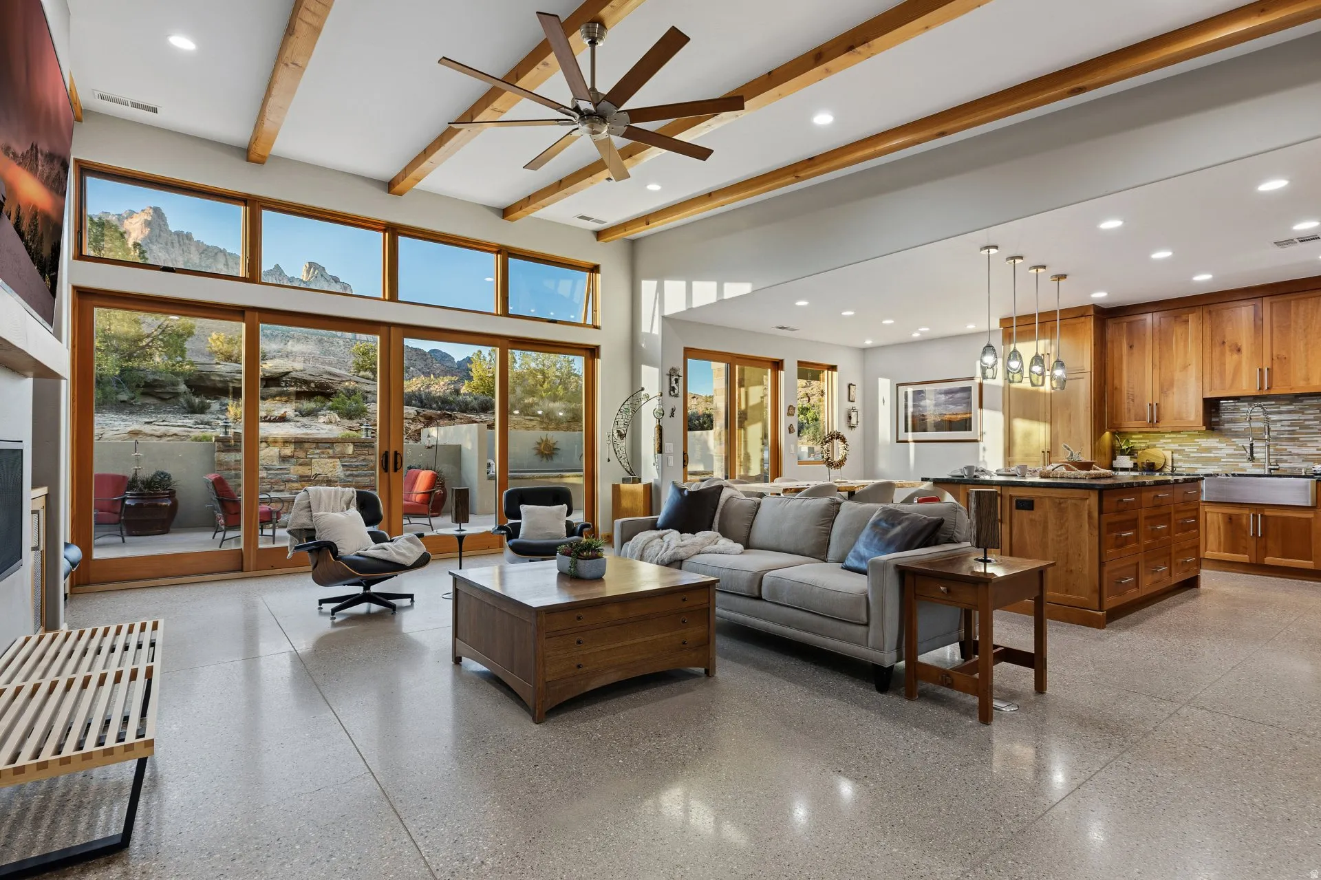 Open-concept living space with exposed wood ceiling beams, a large ceiling fan, and light-toned concrete flooring