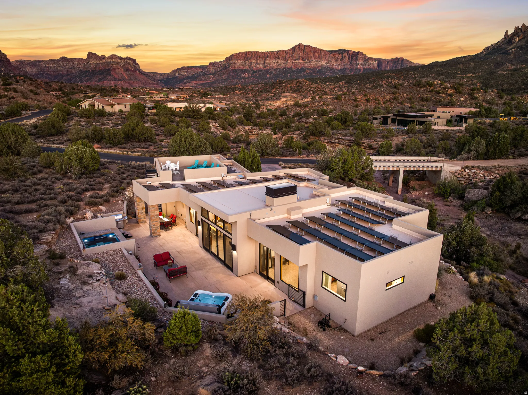 Modern desert architecture featuring multiple outdoor entertaining areas, a private spa, rooftop deck, integrated solar panels, and prominent red rock formations in the distance