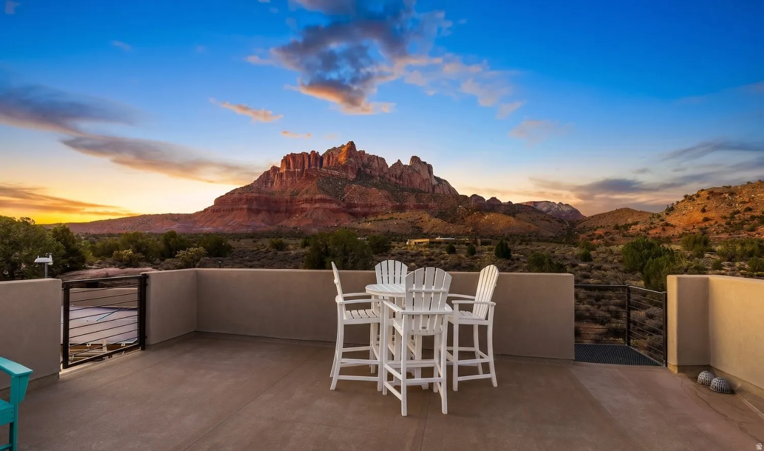 Expansive rooftop patio with a low wall surround and metal railing, featuring a vast mountainous landscape backdrop