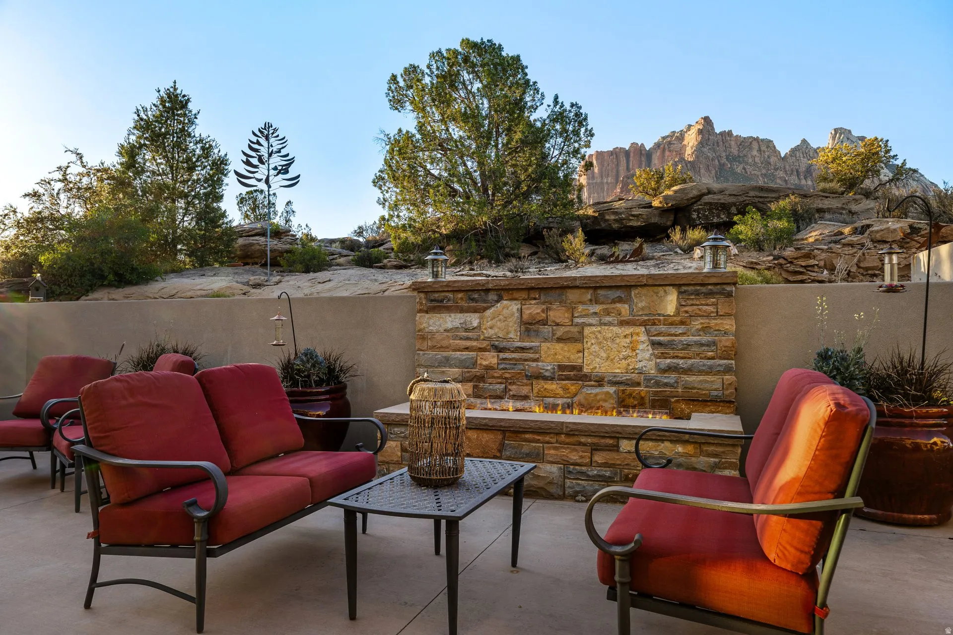 Outdoor patio featuring a built-in stone fire pit, concrete hardscaping, a retaining wall, and natural rock formations