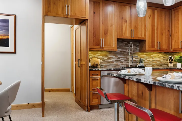 Kitchen featuring wood cabinetry, stainless steel dishwasher, a multi-tone tile backsplash, and a black and white variegated countertop