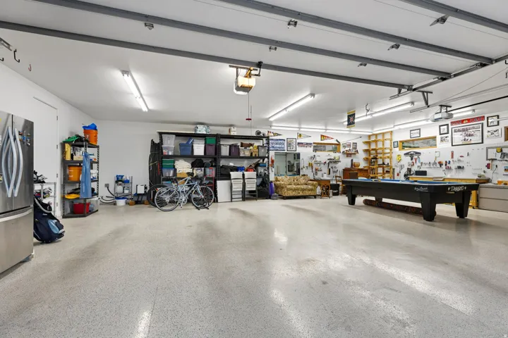 Expansive garage space featuring speckled epoxy flooring, bright overhead fluorescent lighting, and a prominent workbench with shelving