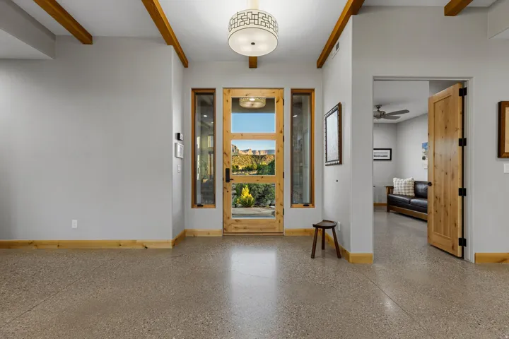 Entryway featuring a wood-frame glass panel door with sidelights, exposed wood ceiling beams, a decorative ceiling light fixture, and polished concrete flooring