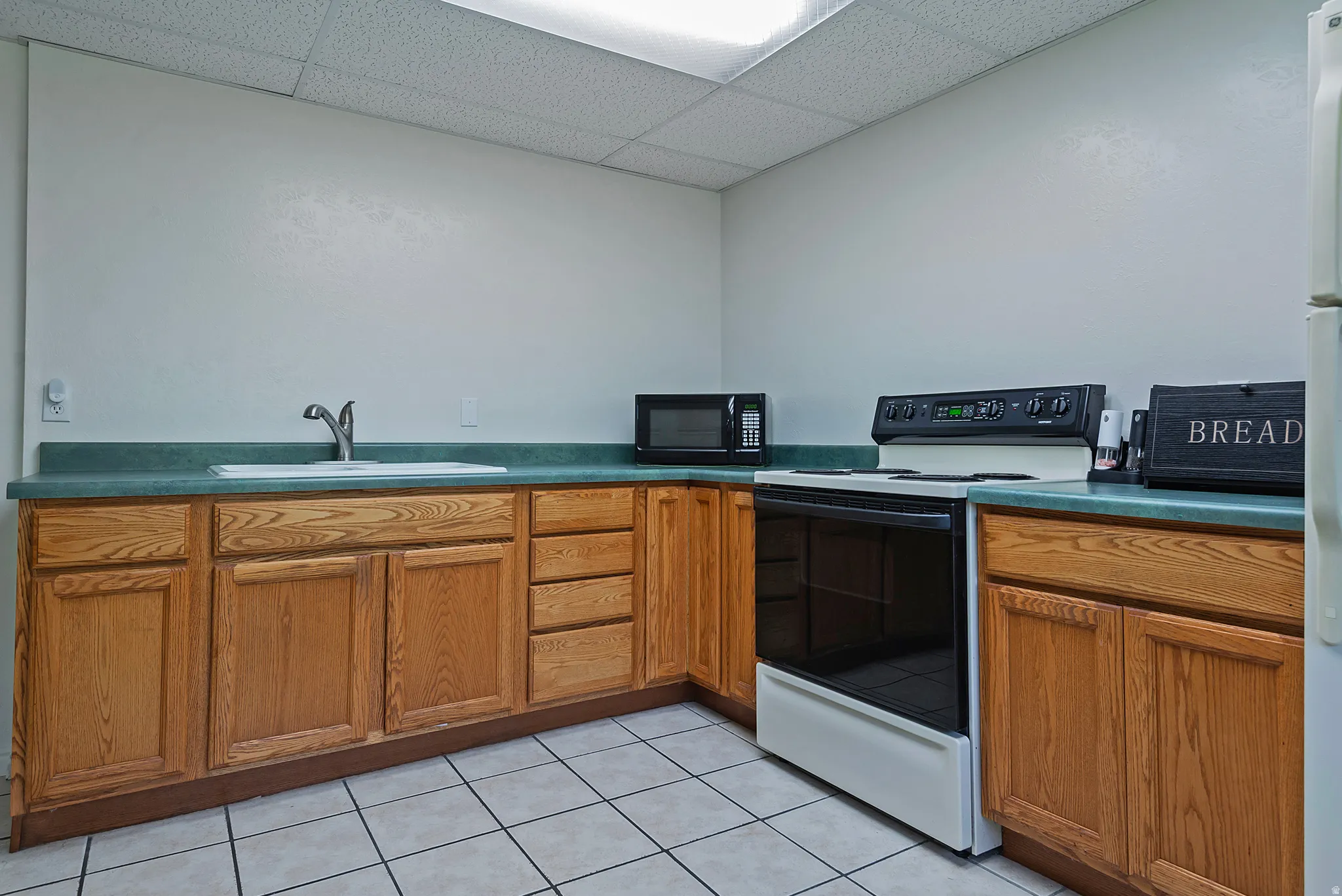 Kitchenette featuring wood-finish cabinetry, a white drop-in sink with a chrome faucet, and a black and white electric range