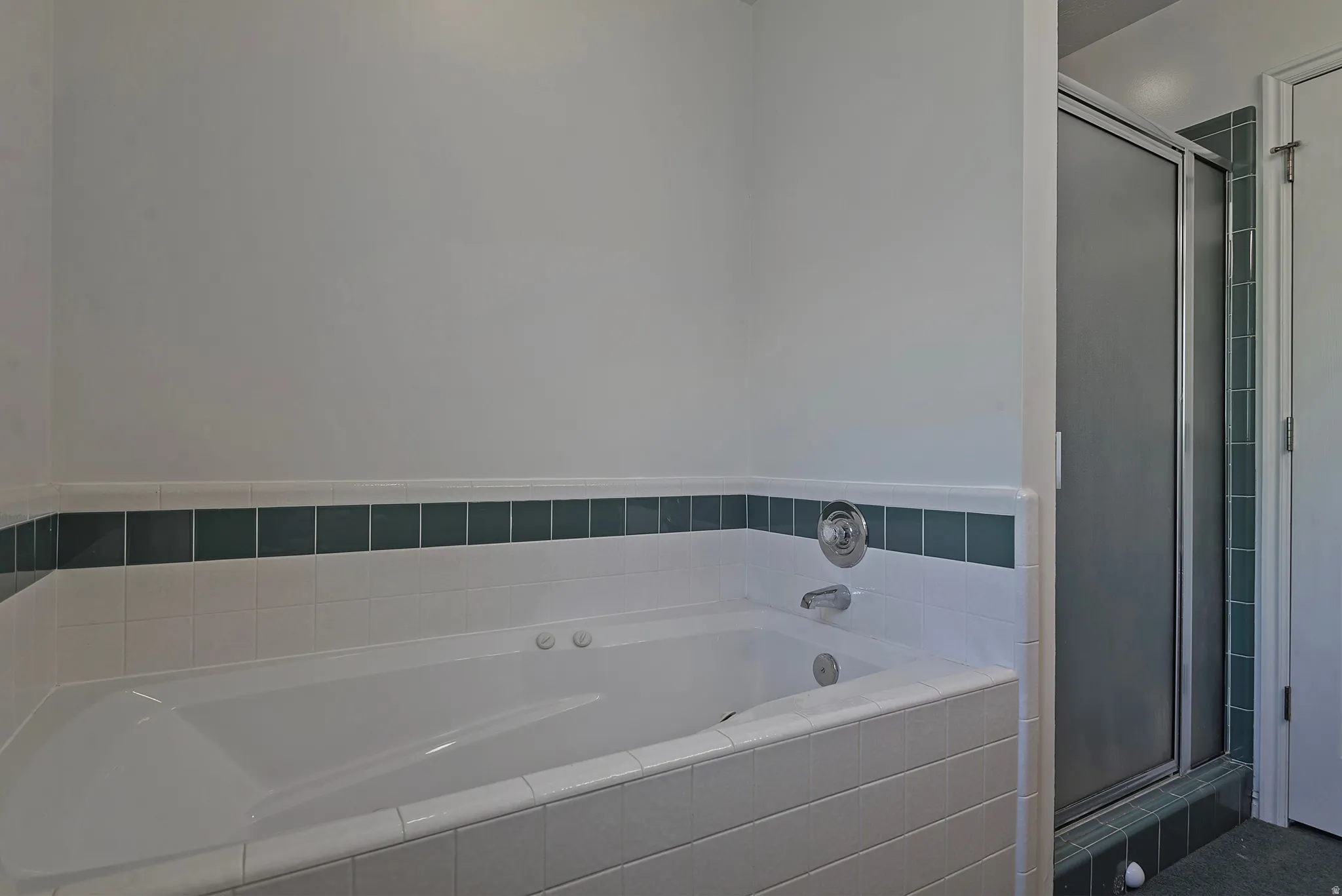 White drop-in jetted bathtub with chrome fixtures and white tile surround
