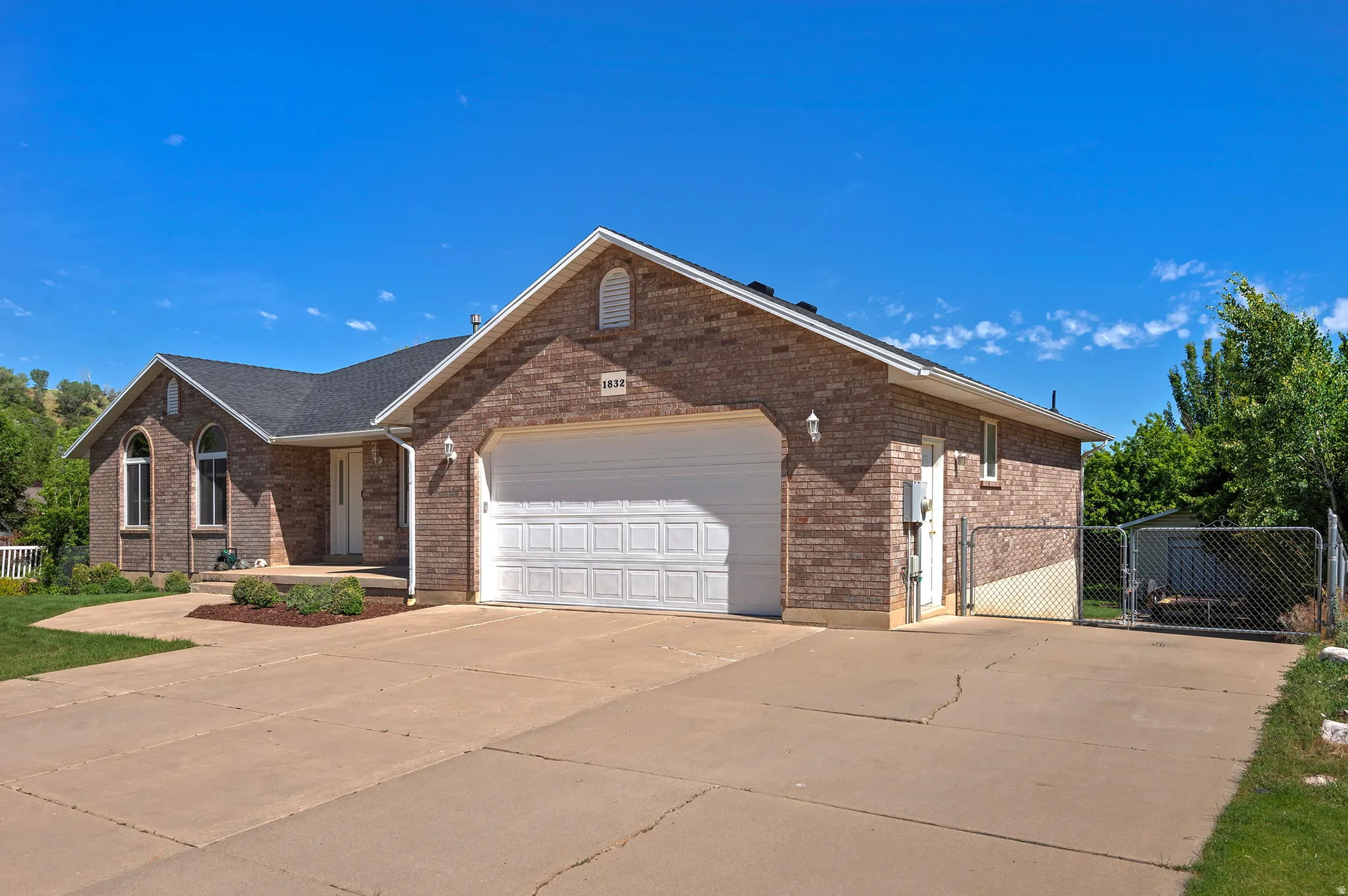 Brick exterior with a prominent two-car garage, rounded front windows, a covered entry, and a side chain-link fence