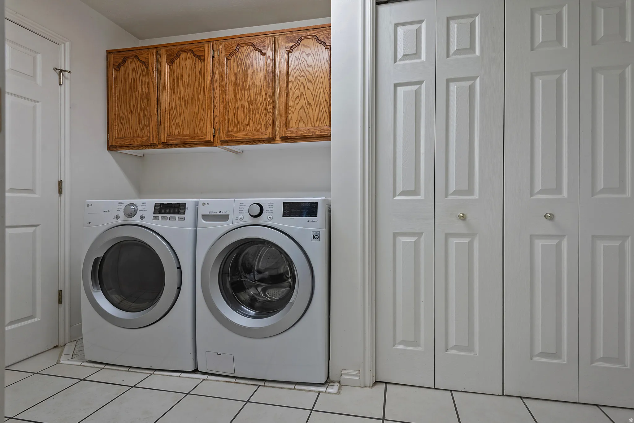 Laundry area featuring overhead wood-finish cabinetry, tile flooring, and bi-fold doors