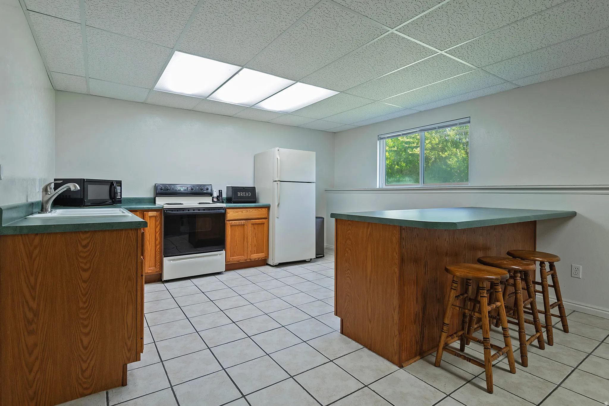 Kitchen space featuring wood-finish cabinetry, light-toned tile flooring, and a drop ceiling with recessed lighting