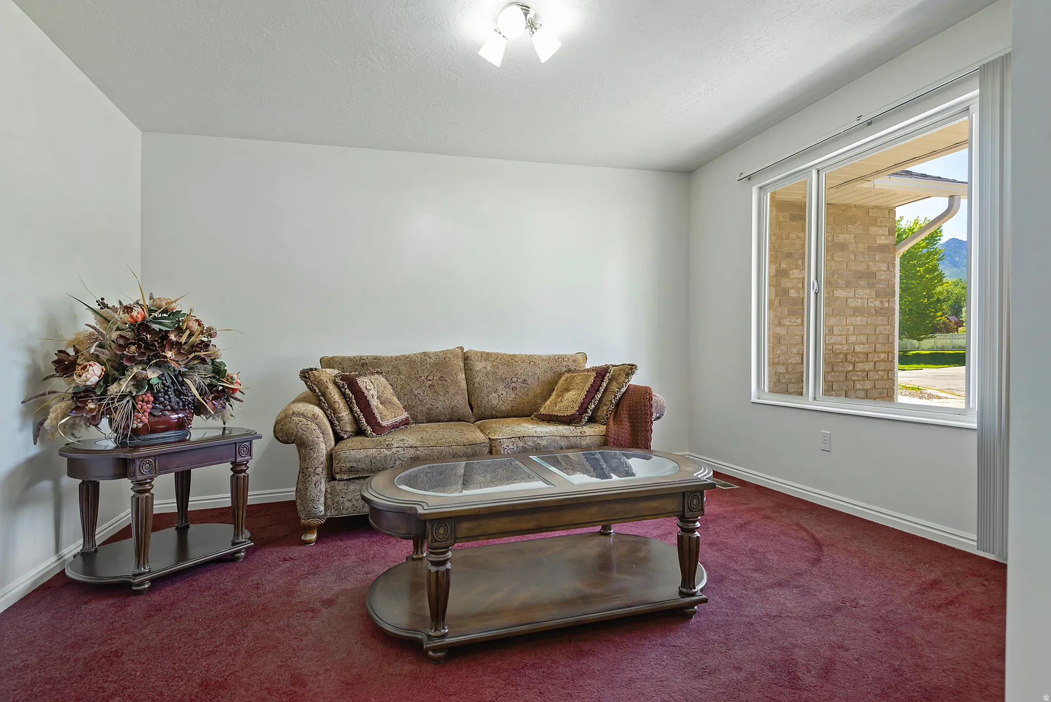 Spacious living area featuring light-colored walls, red carpet flooring, a large window, and white trim