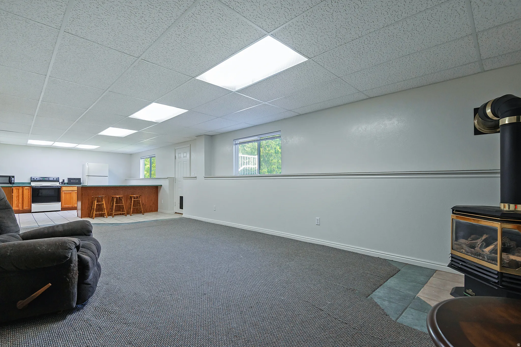 Spacious lower level featuring a modern stove fireplace with a tile hearth, a wood-finish bar, recessed lighting, wood-finish cabinetry, and white appliances