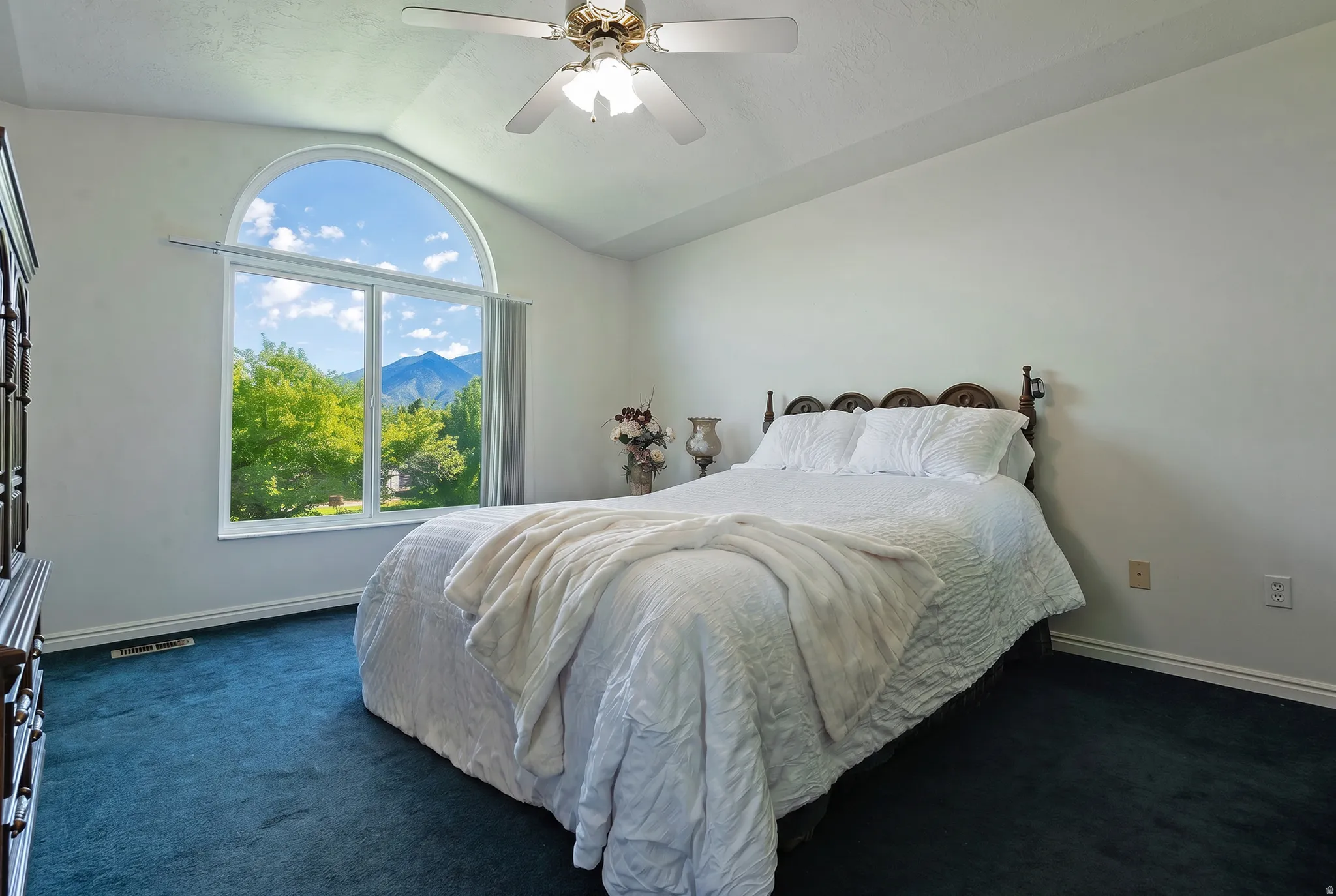 Vaulted ceiling with a ceiling fan, arched window with mountain scenery, and dark blue carpet flooring