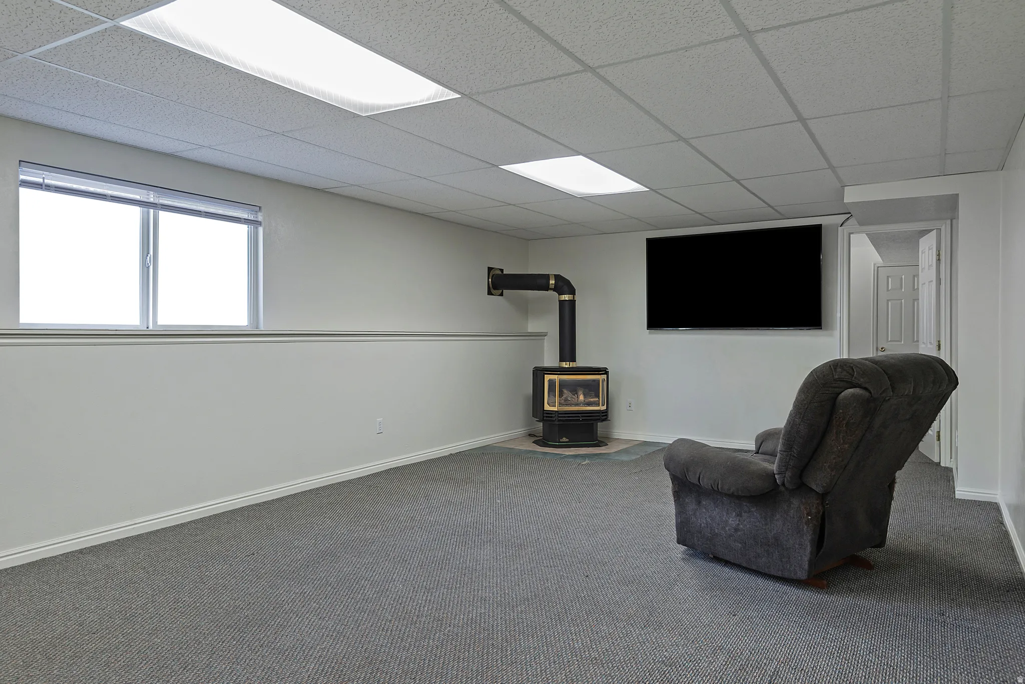 Carpeted entertainment area featuring a mounted television and a built-in wood-burning stove with a black pipe vent