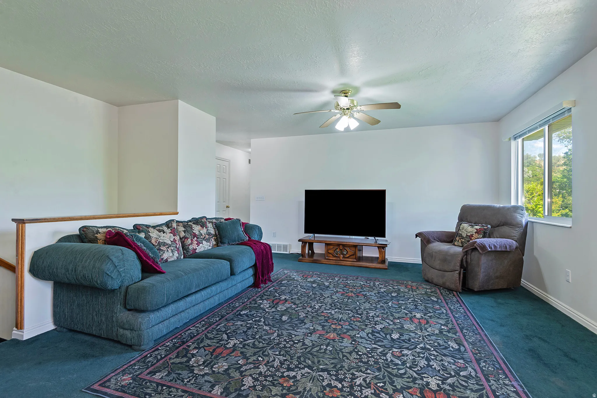 Spacious living area featuring light-toned walls, a ceiling fan with integrated lighting, and a large window providing natural light