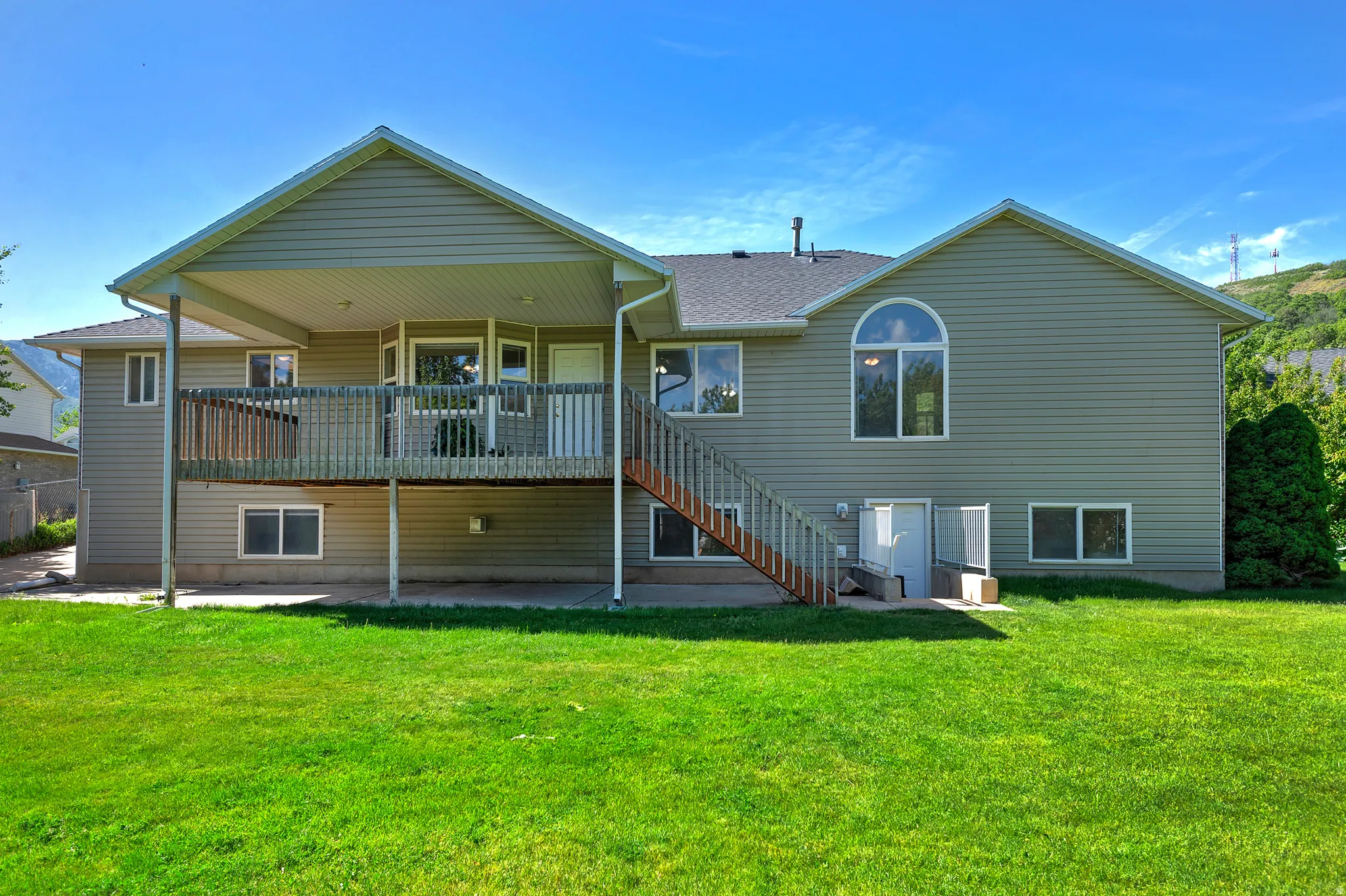 Expansive backyard featuring a manicured lawn, a large upper deck with a covered portion, and a full walk-out basement entrance