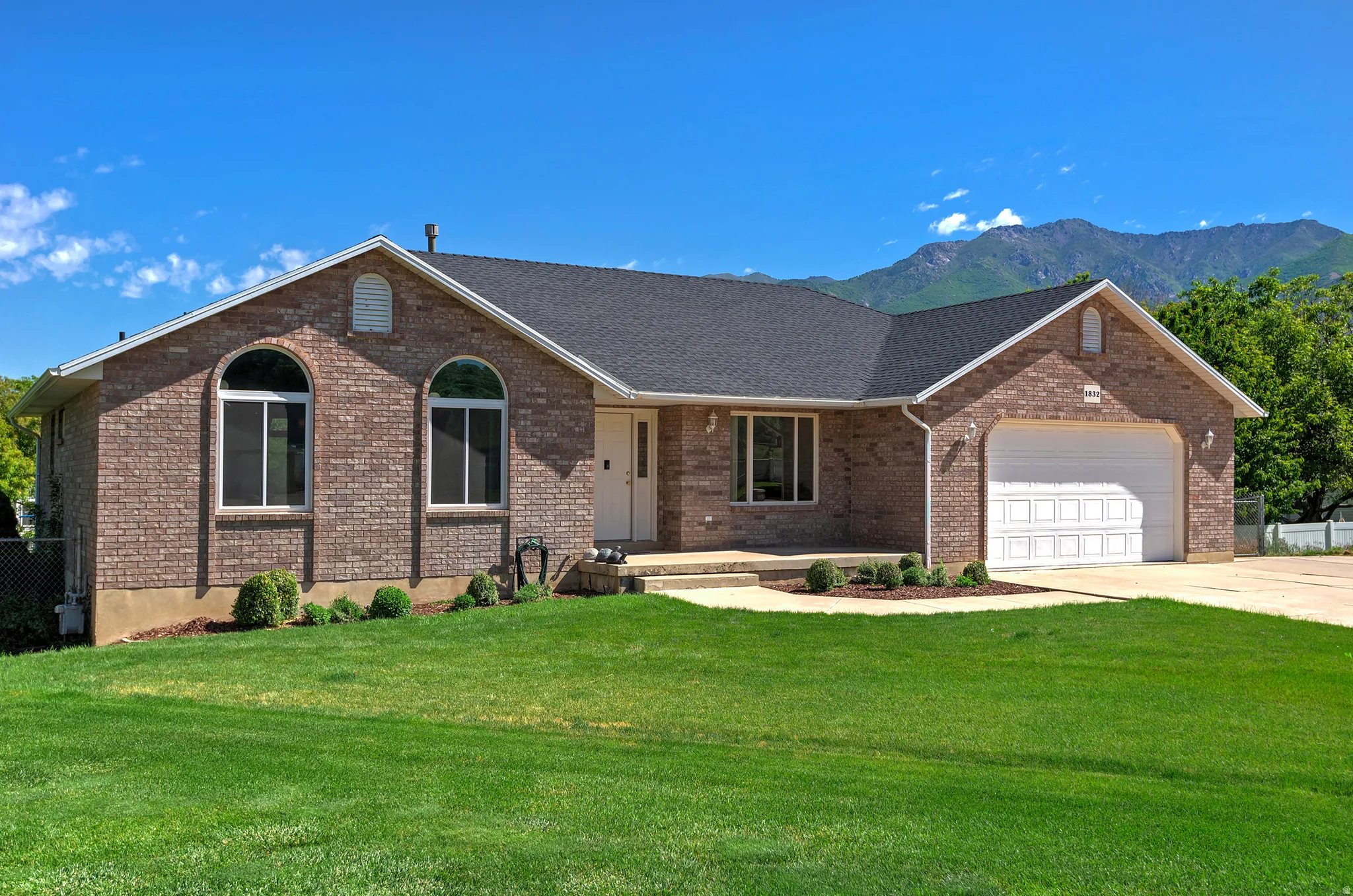 Brick exterior residence featuring a dark shingle roof, arched windows, and an attached two-car garage