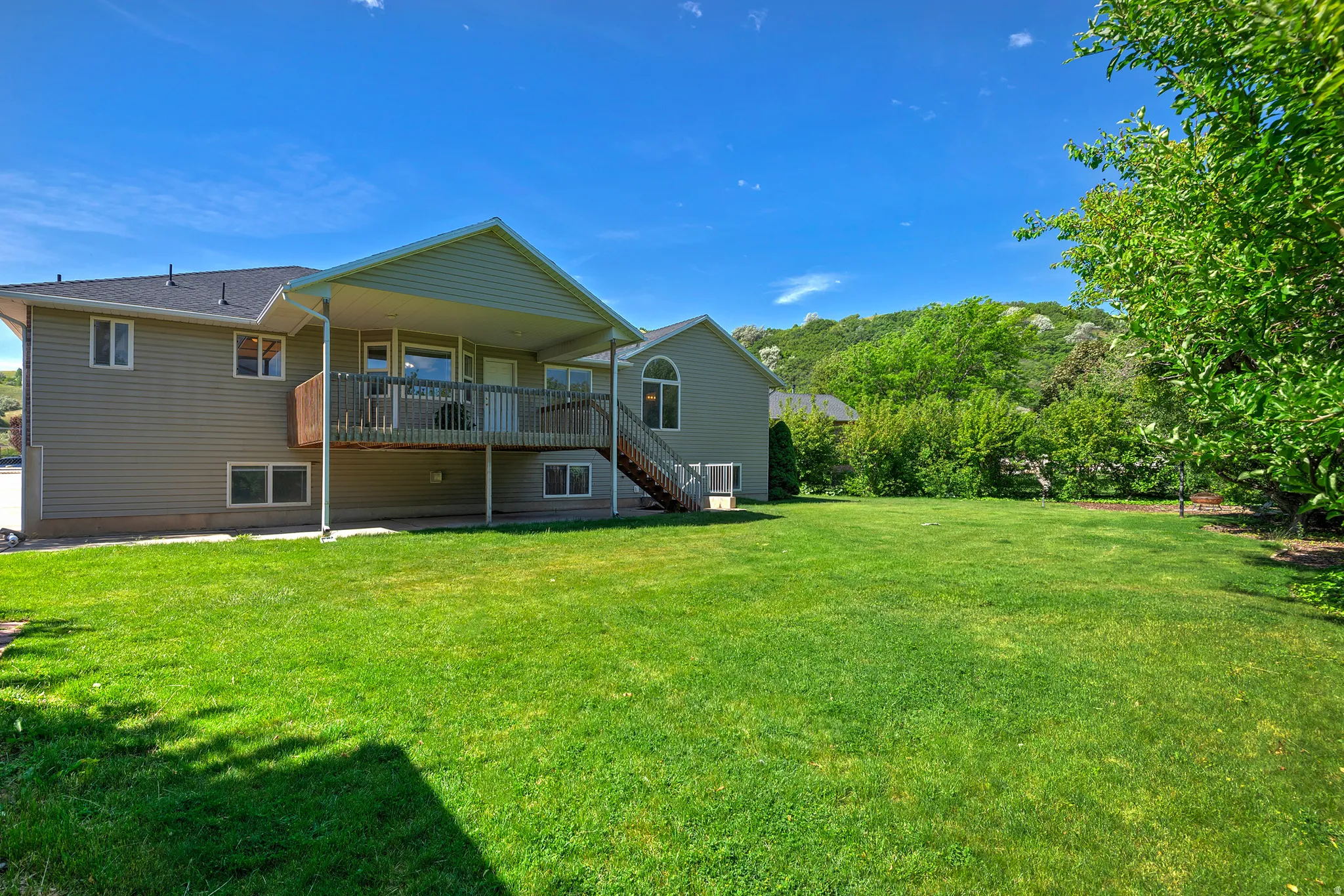 Expansive green lawn with a covered deck, wood handrails, and exterior stairs