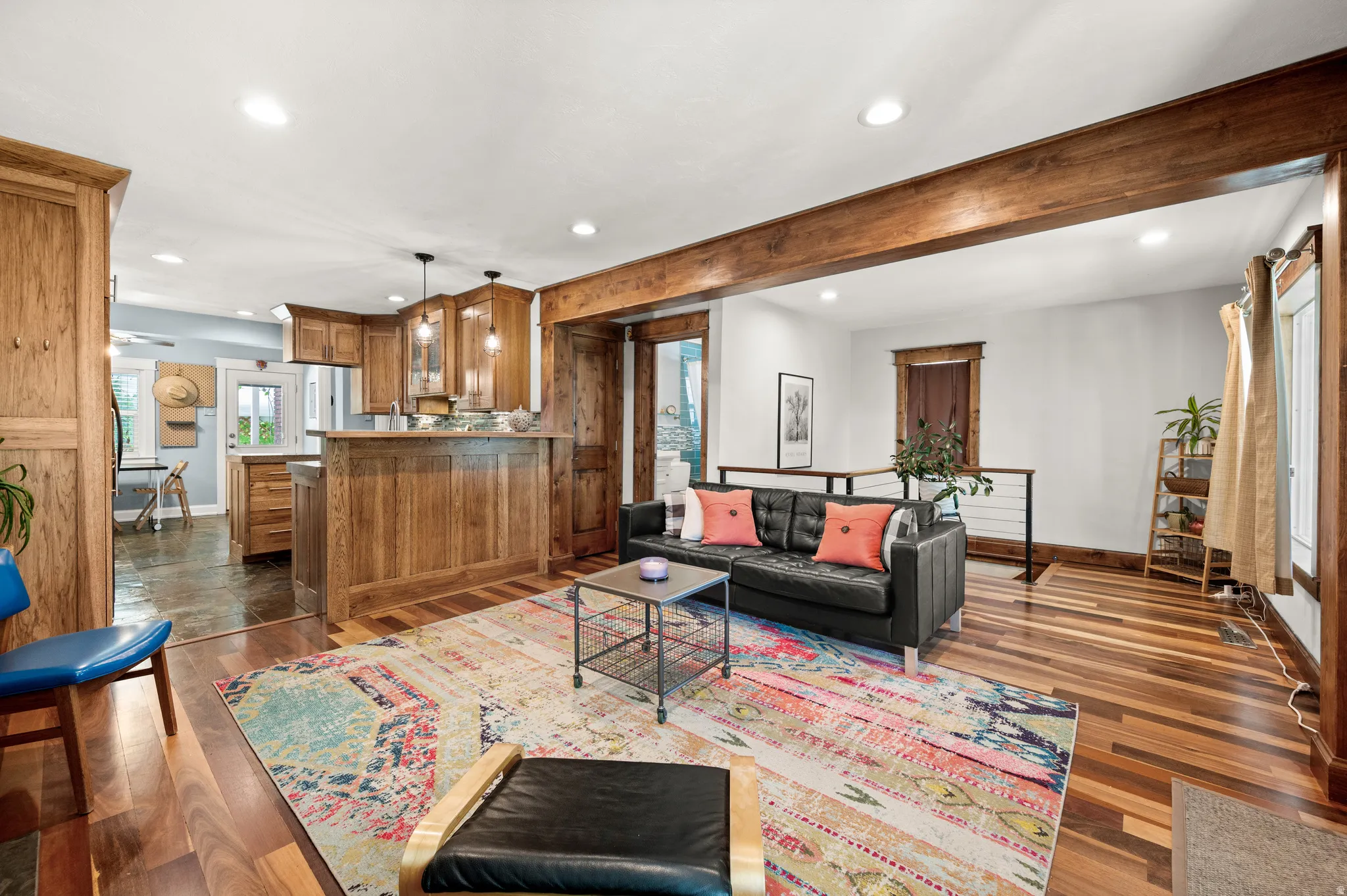 Open-concept living area featuring rich wood flooring, a substantial exposed ceiling beam, and a kitchen bar with wood-finish cabinetry