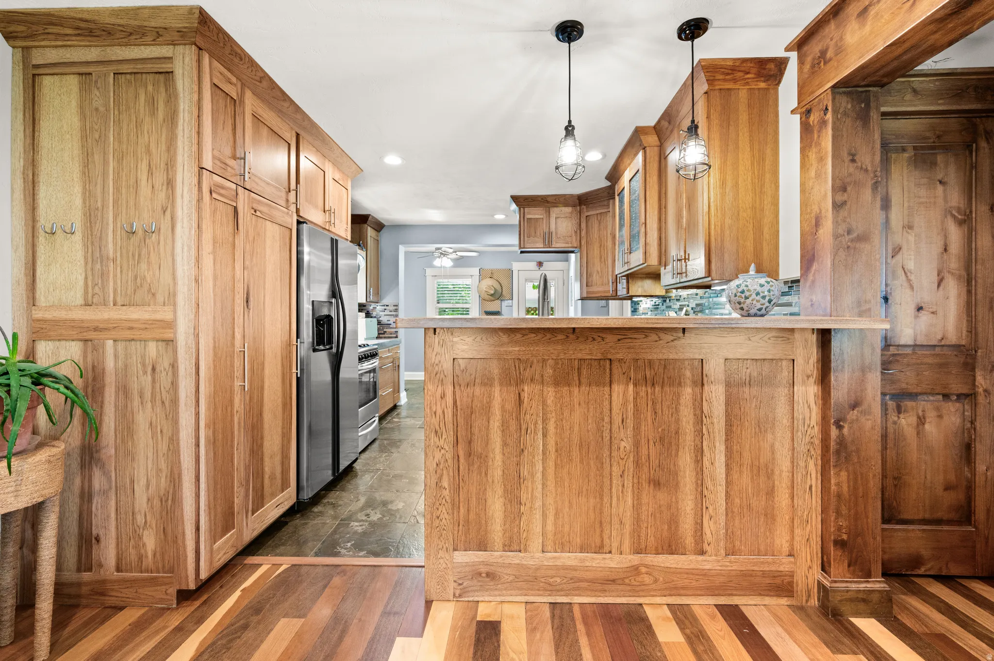 Kitchen featuring natural wood cabinetry, stainless steel appliances, a multi-tone tile backsplash, and overhead pendant bar lighting