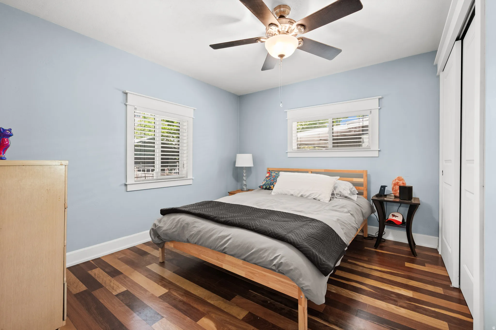 Primary bedroom featuring a ceiling fan with integrated lighting, two windows with white blinds, and a built-in closet with sliding doors