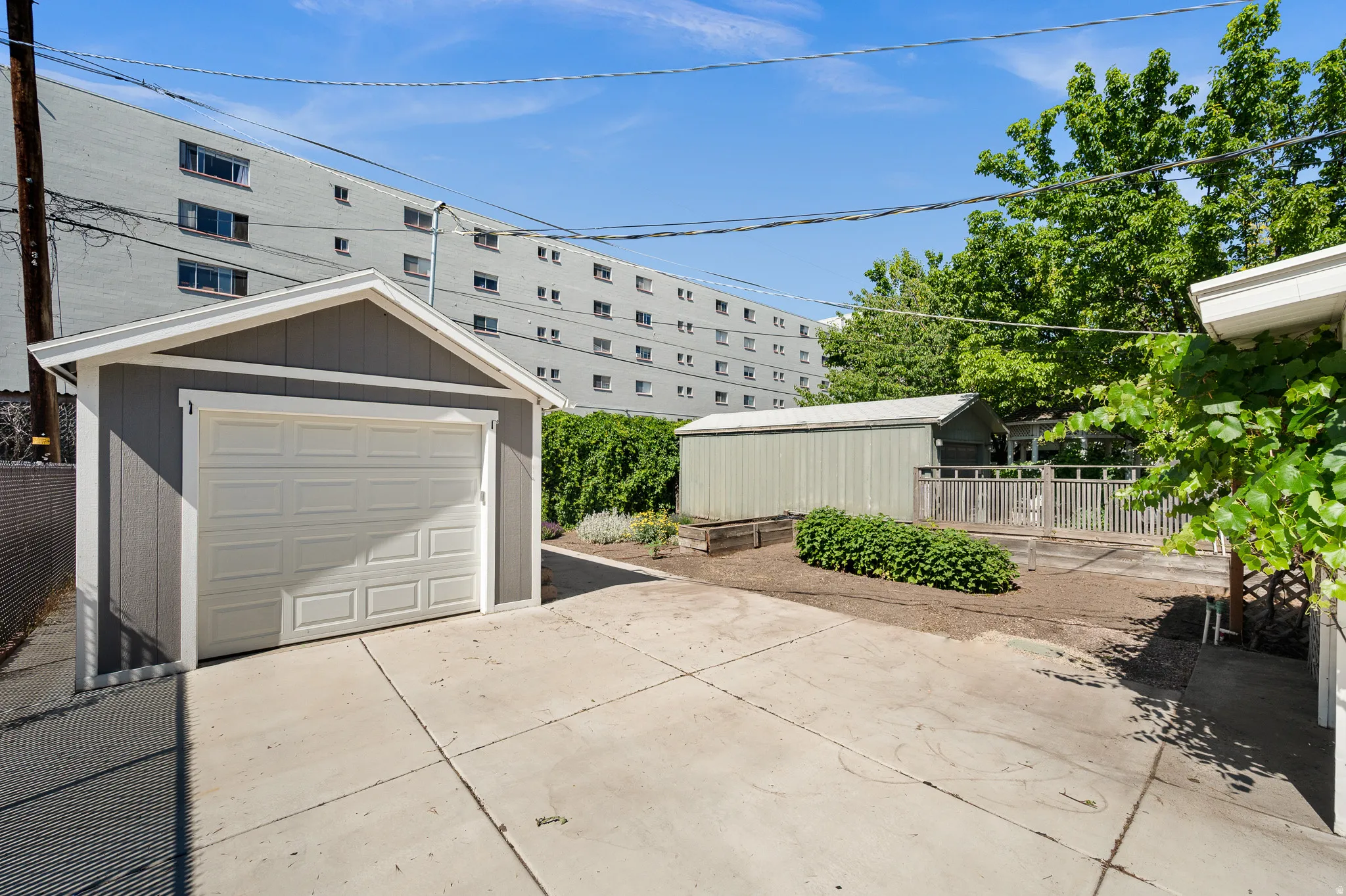 Newer detached garage featuring a paneled overhead door and gray siding, newer concrete driveway, backyard garden area