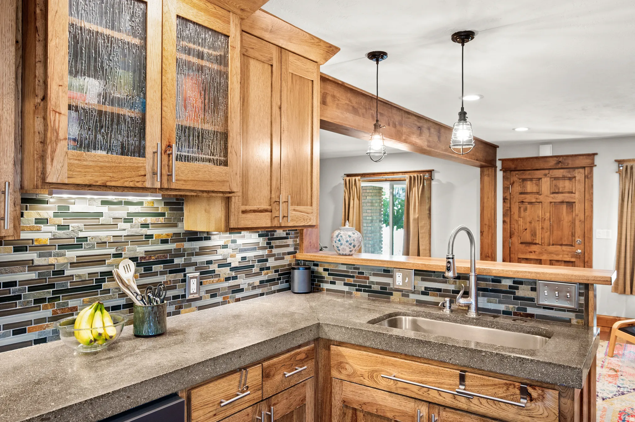 Kitchen featuring custom wood cabinetry with glass front cabinets, concrete countertops, a tile backsplash, and a stainless steel undermount sink with a gooseneck faucet