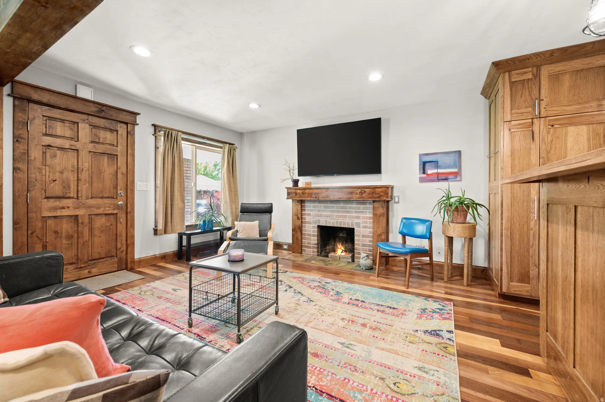 Living room featuring large window, wood-finish flooring, a brick fireplace with a wood mantel, recessed lighting, and a six-panel wood door