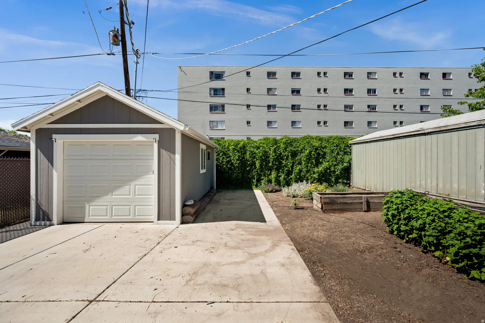 Newer detached garage with a paneled garage door and a side window, featuring a newer concrete driveway, and garden areas