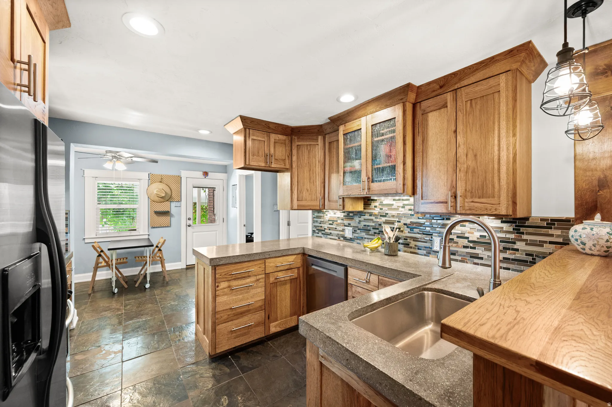 Kitchen featuring natural wood cabinetry, multi-toned tile backsplash, and slate-finish flooring, dining area and door to backyard
