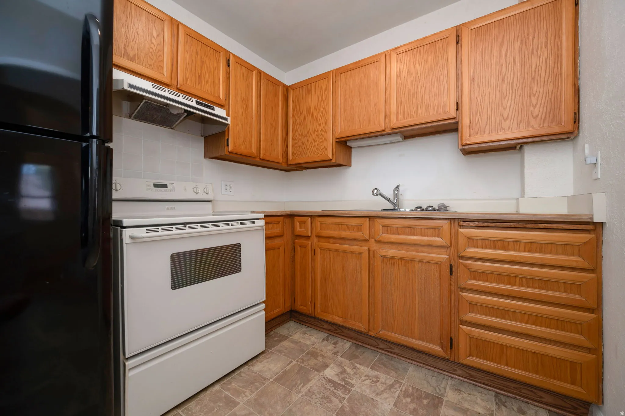 Kitchen featuring wood-finish cabinetry, a white electric range, and a black refrigerator