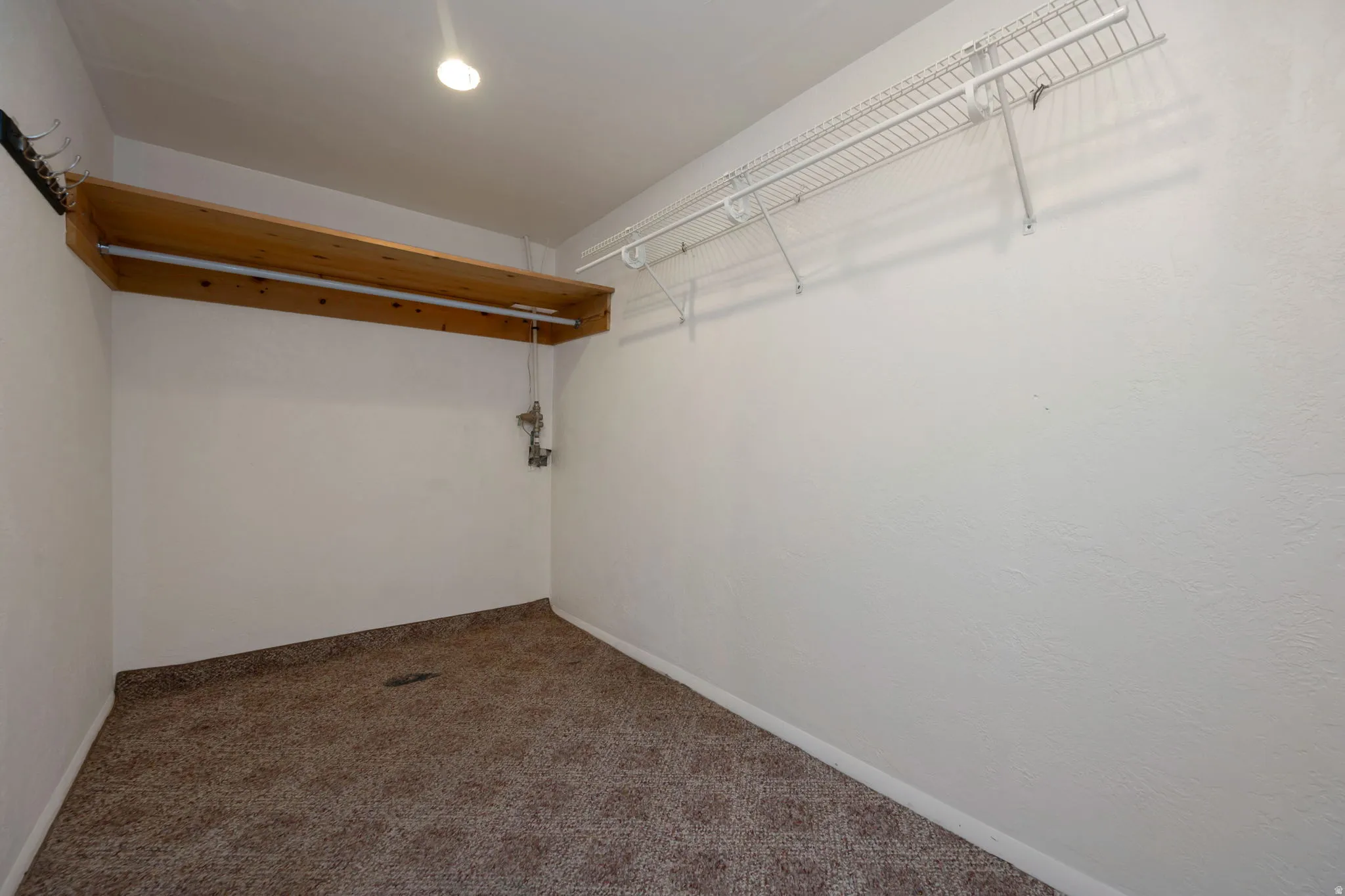 Carpeted room with a wooden shelf and hanging rod, complemented by white wire shelving