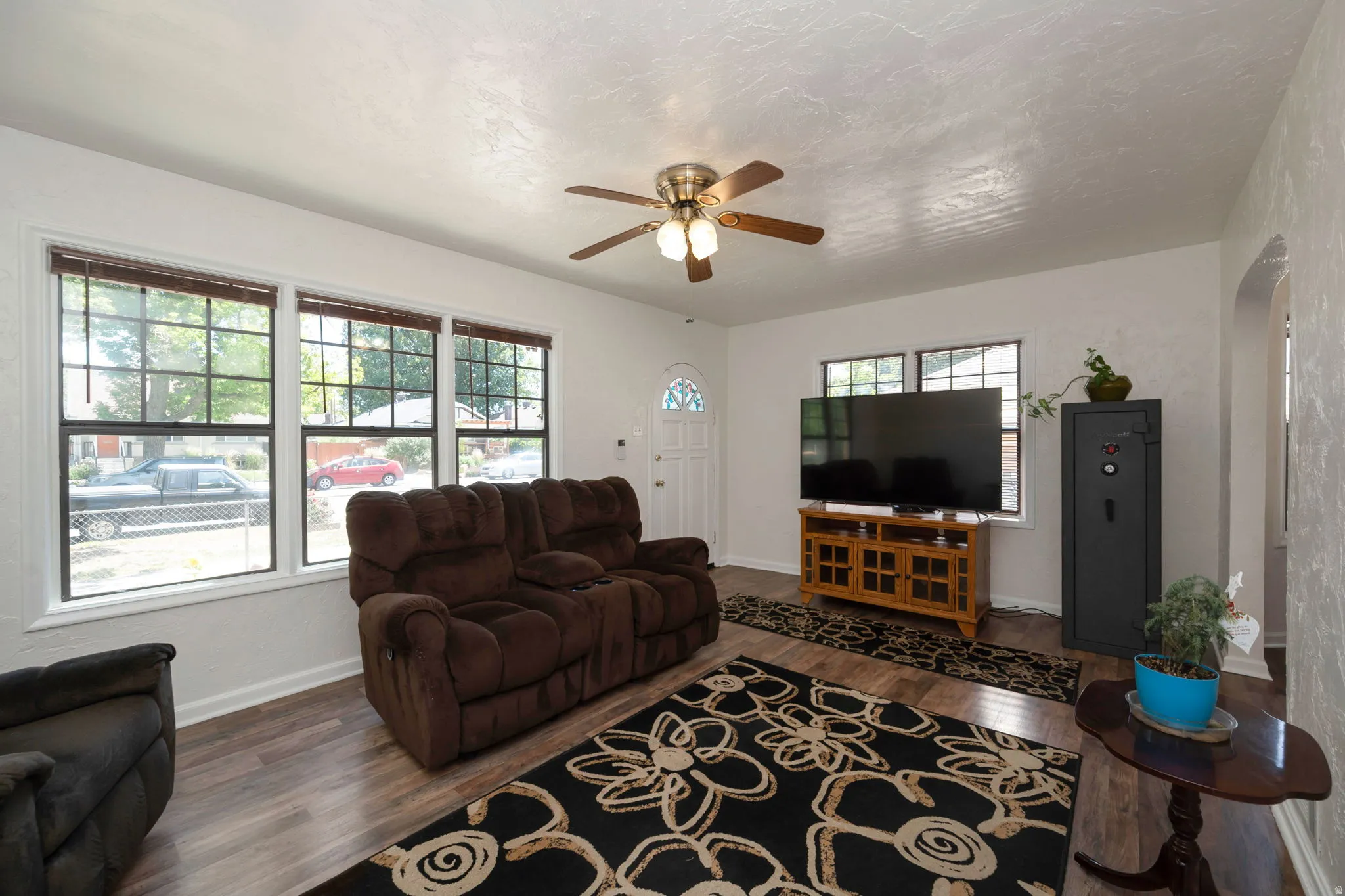 Living area featuring wood-finish flooring, white walls, and a ceiling fan with integrated lighting