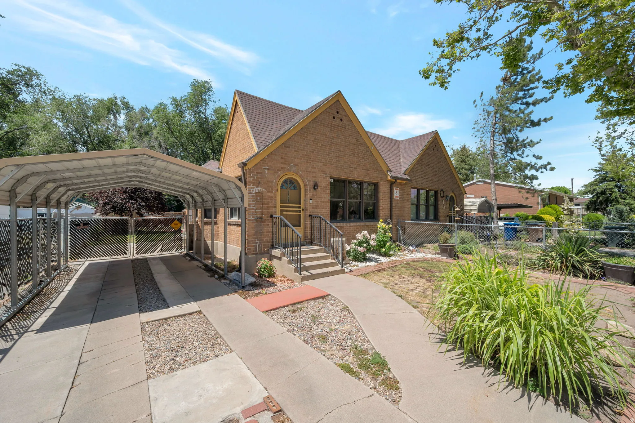 Brick exterior featuring an arched entryway, covered carport, concrete driveway, and mature landscaping