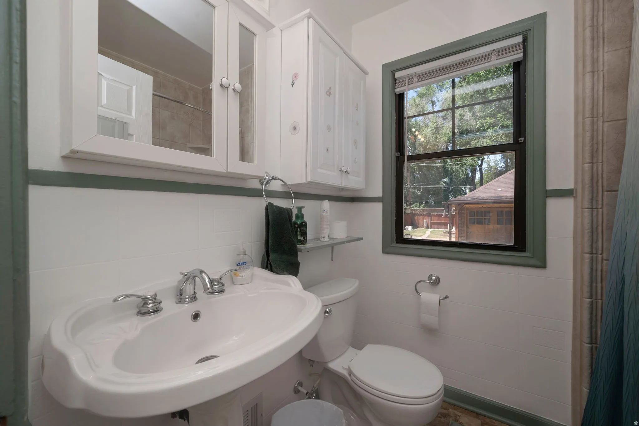Pedestal sink with chrome fixtures, medicine cabinet with mirrored doors, and white paneled upper cabinetry