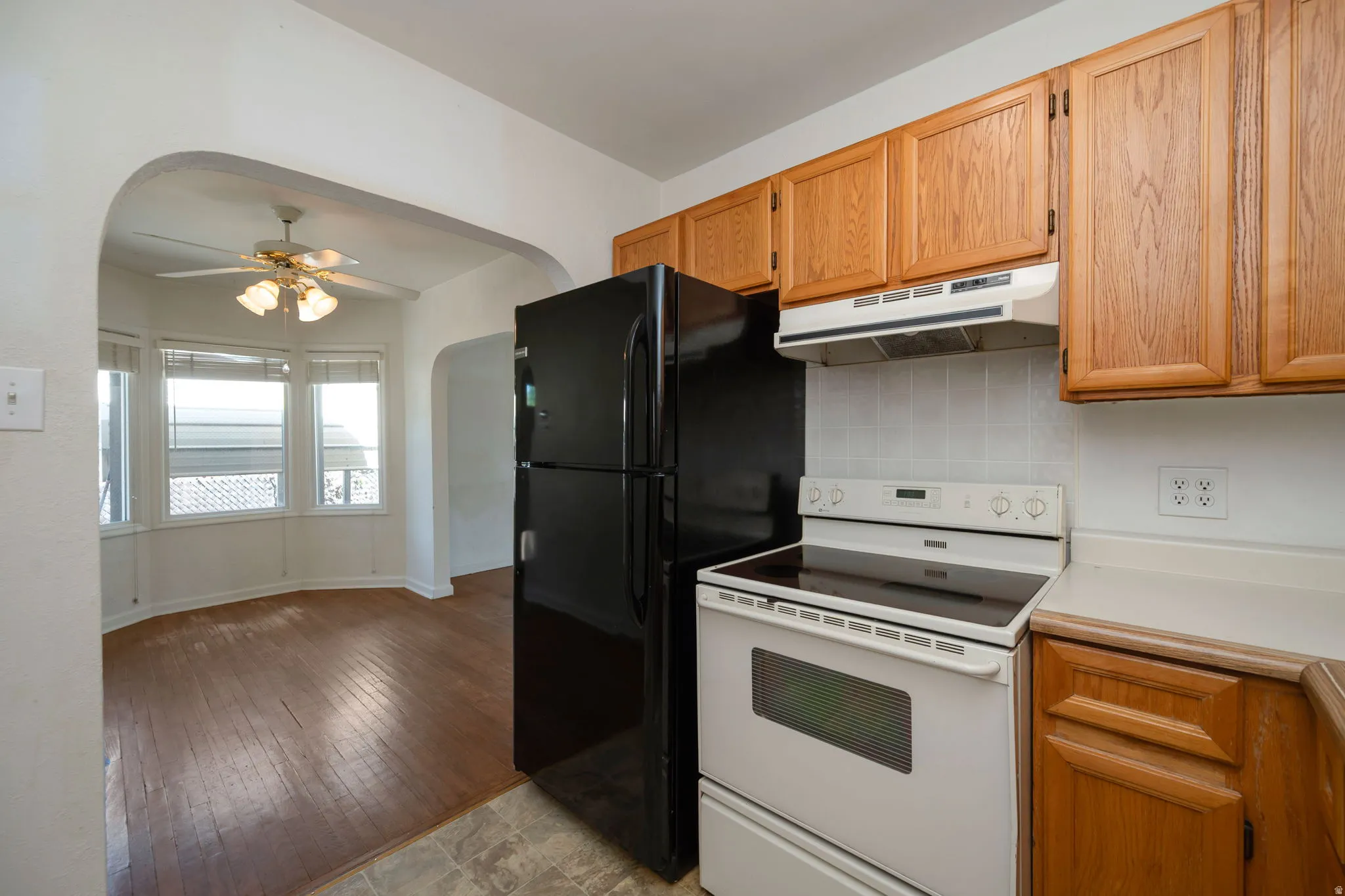 Kitchen featuring wood-finish cabinetry, white tile backsplash, and built-in white appliances