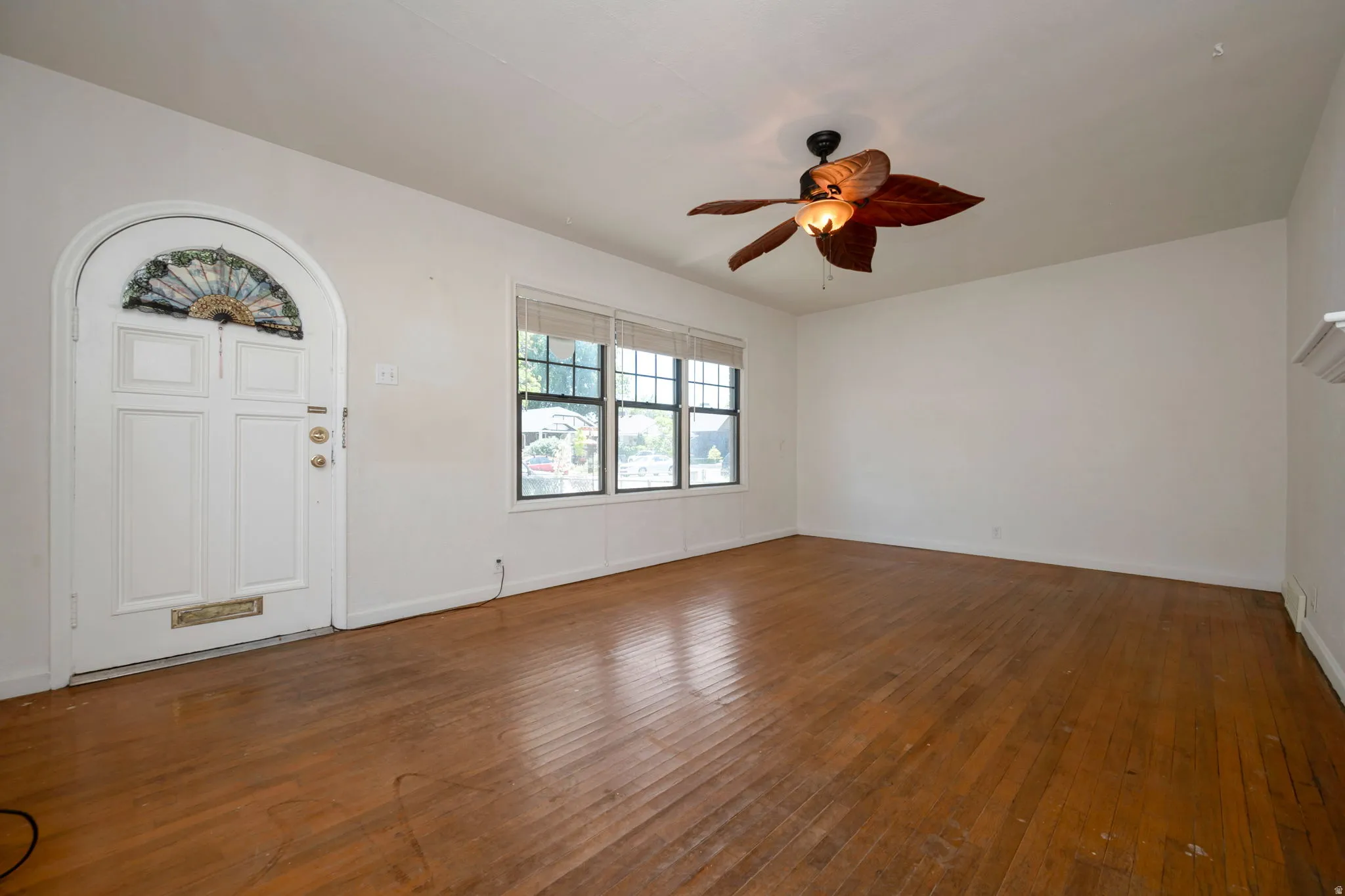 Spacious interior featuring wood-finish flooring, a decorative arched entryway with a fanlight, multiple windows, and a ceiling fan