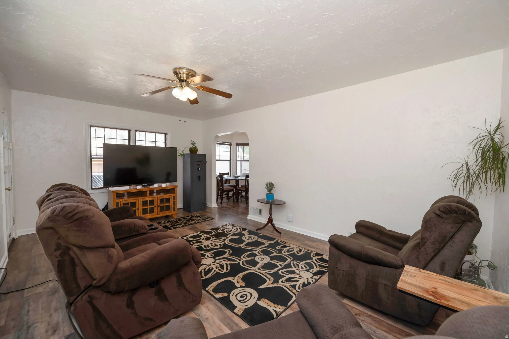Living area featuring wood-finish flooring, a ceiling fan with integrated lighting, and multiple windows