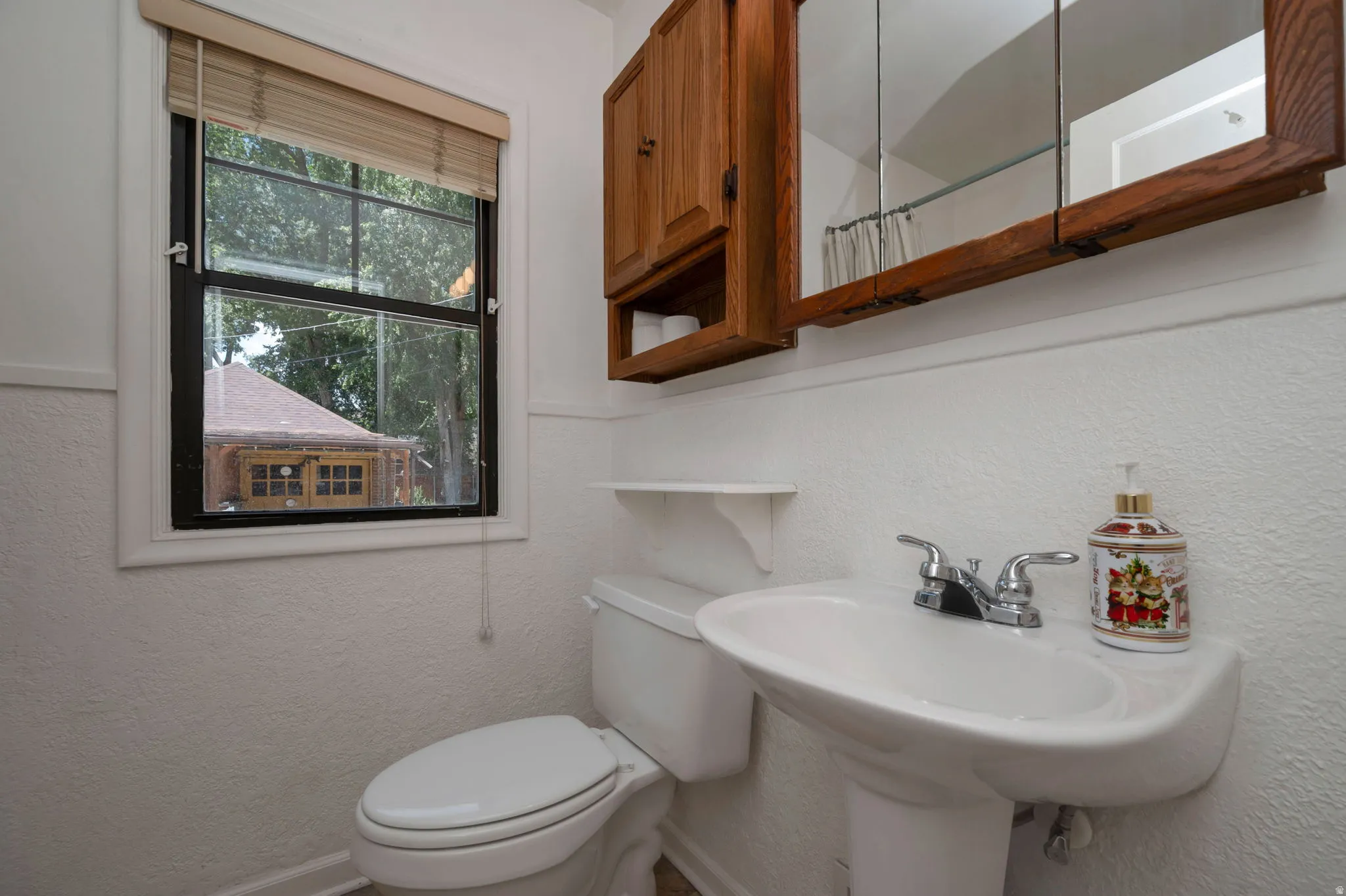 Pedestal sink with chrome fixtures, wood-framed medicine cabinet, and a single-pane window with a woven blind