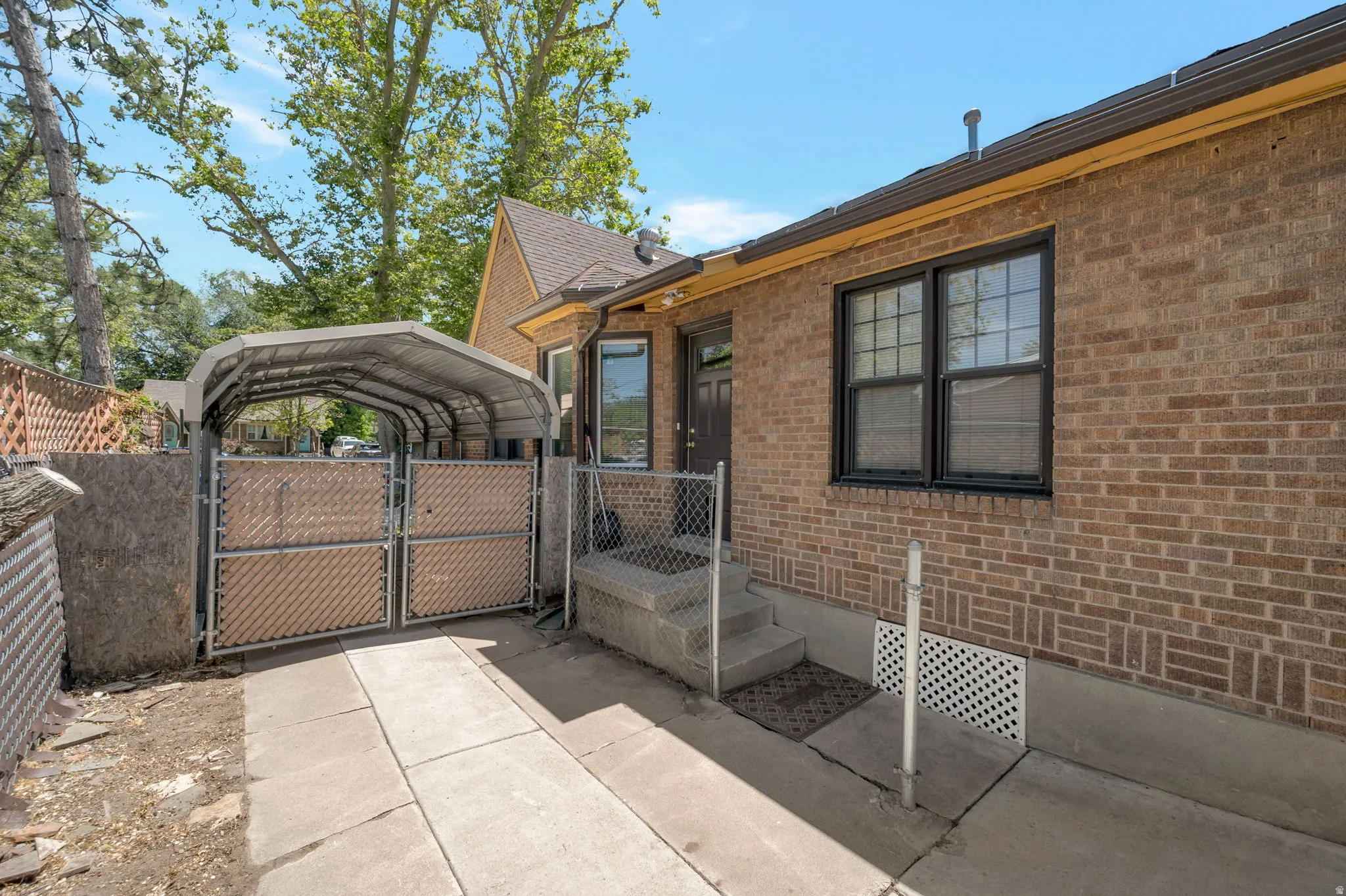 Brick exterior with a metal carport structure and secure chain-link fencing