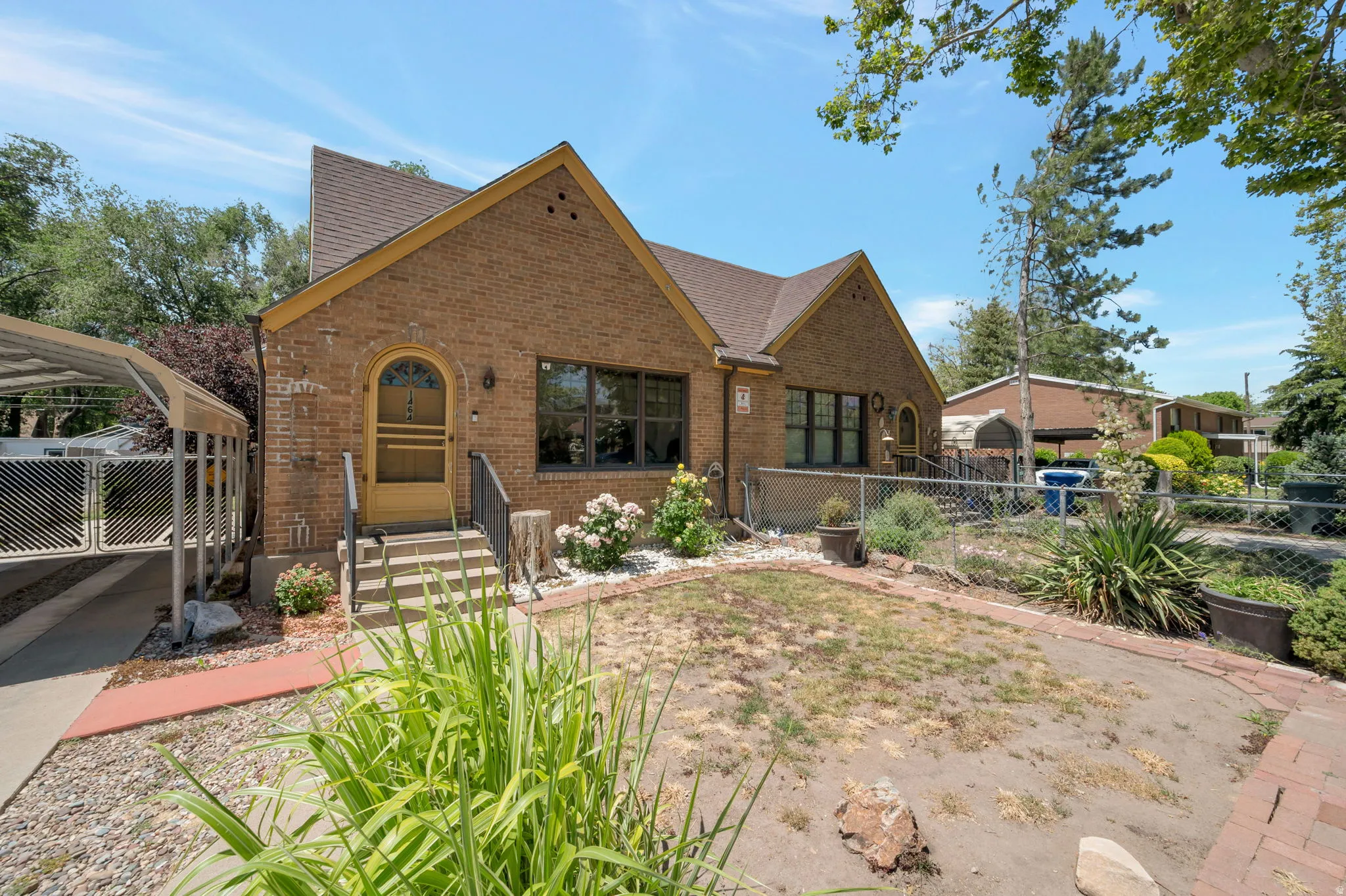 Brick exterior home featuring a covered carport, arched entry door, mature landscaping, and an established front walkway