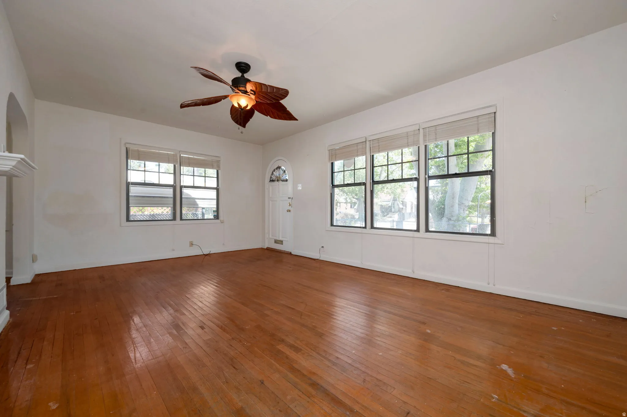 Wood-finish flooring throughout, featuring a decorative ceiling fan and multiple window units with natural light