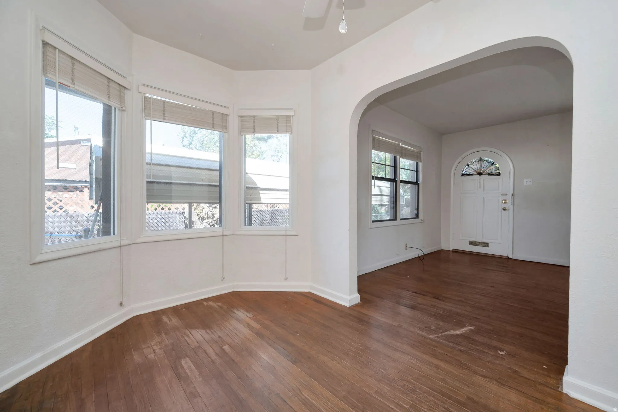 Living area featuring a bay window with three large panes, wood-finish flooring, and an arched doorway opening to an entryway with a decorative front door