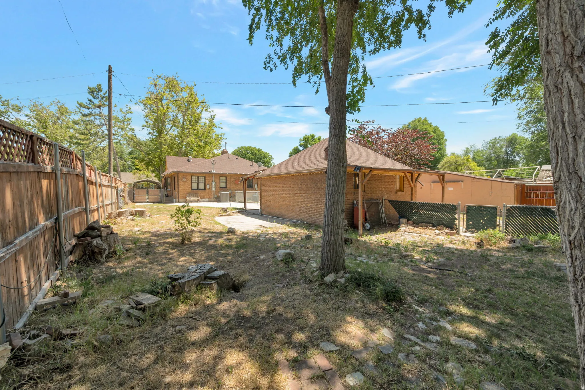 Expansive backyard featuring mature trees, a wooden privacy fence, and a detached brick structure with an attached covered patio