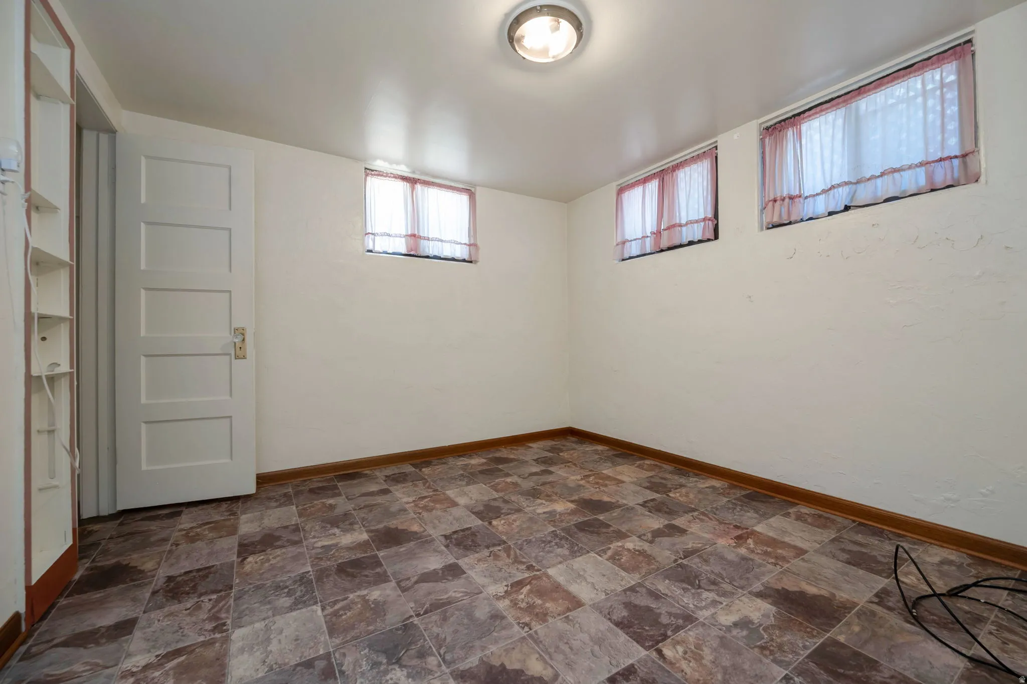 Spacious room featuring patterned tile flooring, multiple windows, a paneled door, and built-in shelving