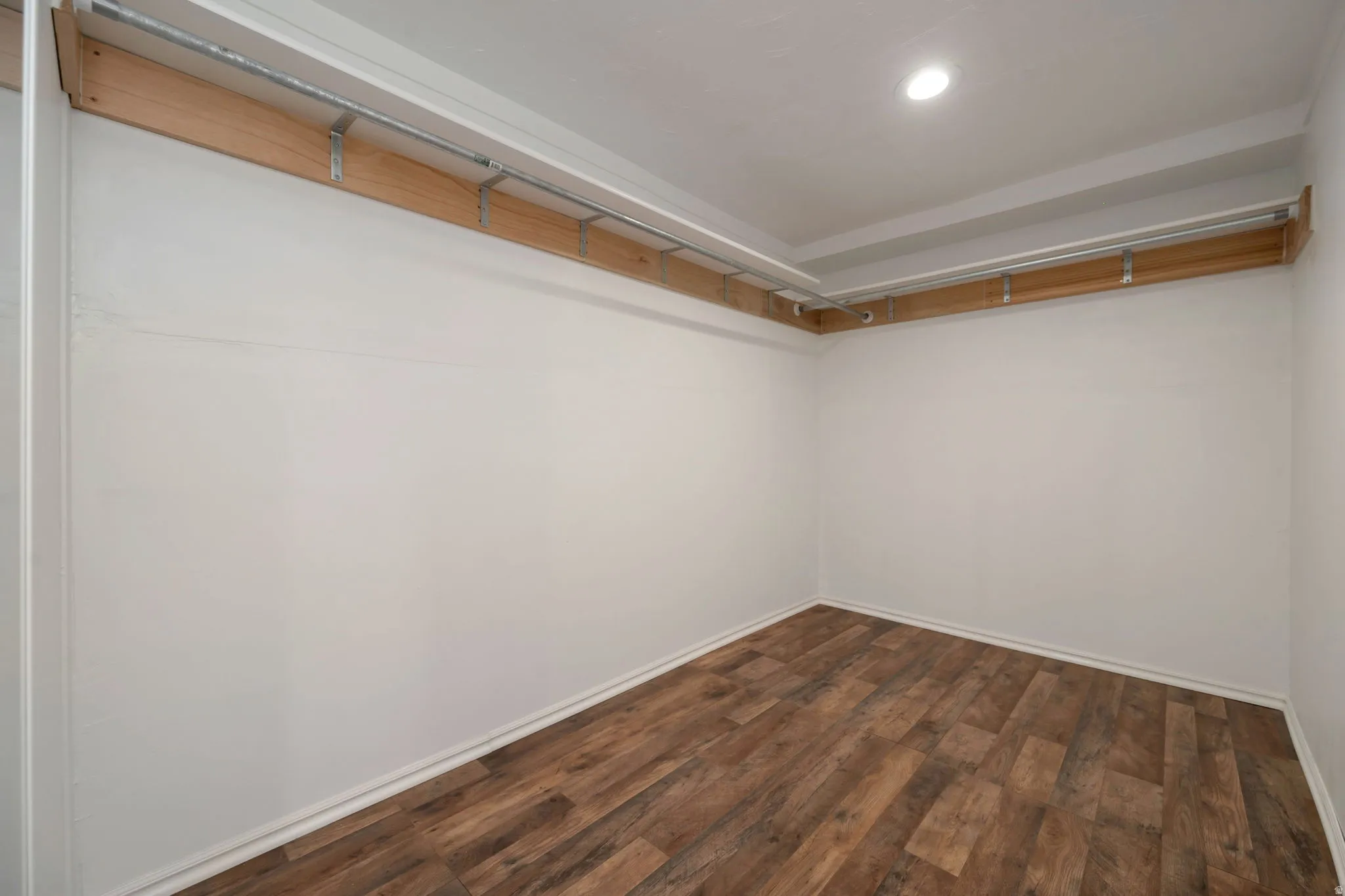 Spacious walk-in closet featuring wood-finish flooring, white walls, and built-in wood shelving with metal hanging rods