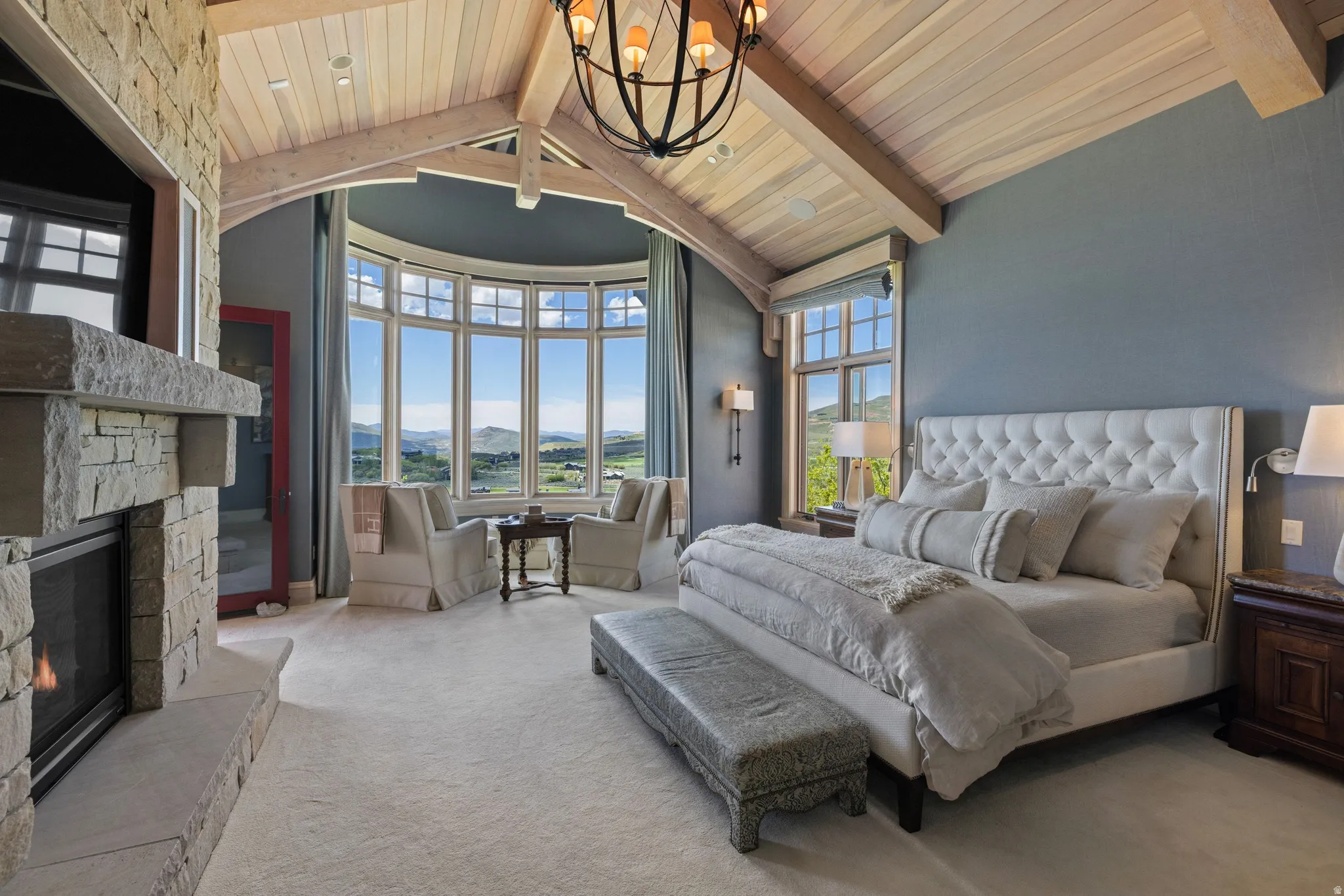 Spacious room featuring vaulted wood-paneled ceilings with exposed beams, a stone fireplace, and a curved bay window with multiple panes