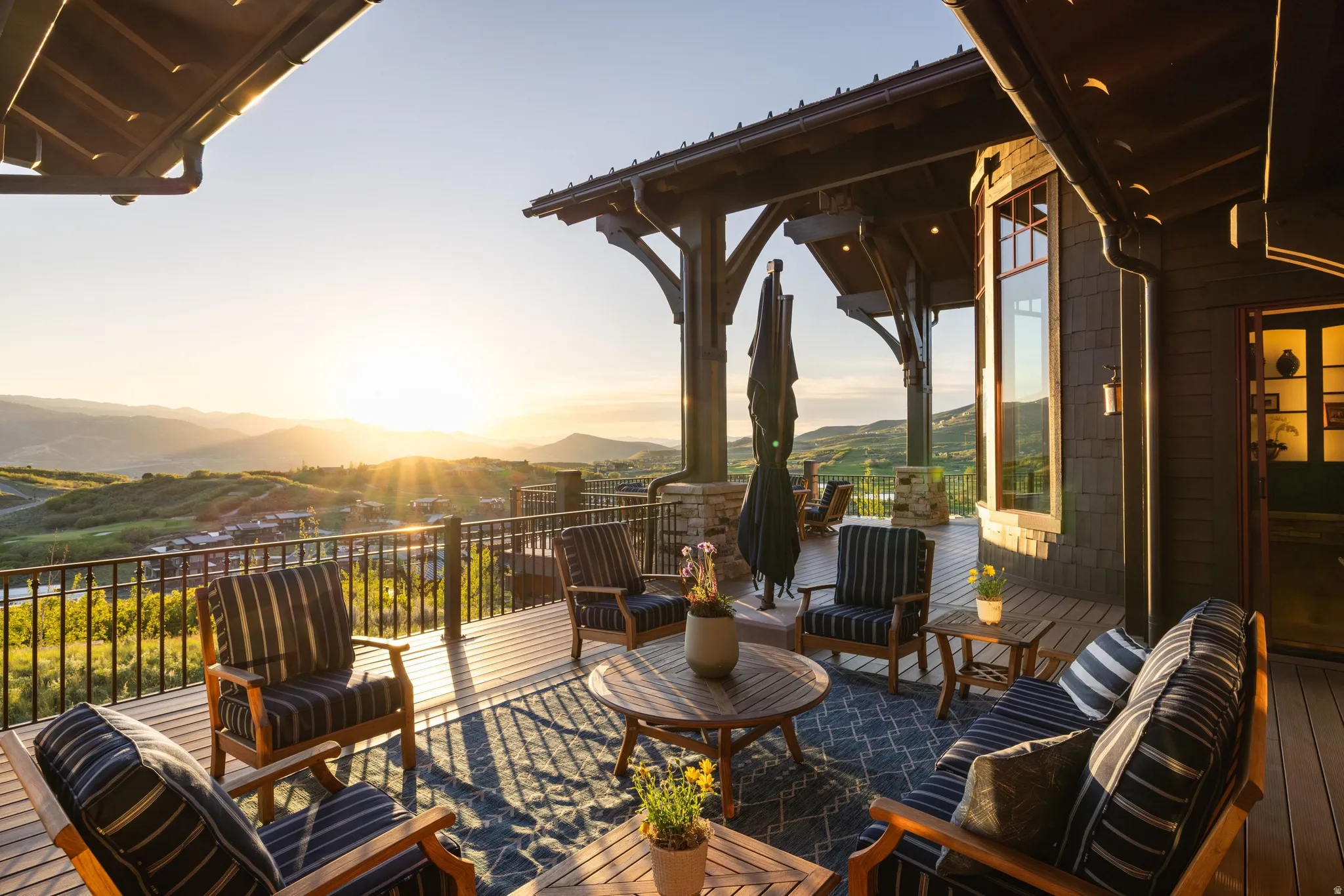 Expansive outdoor deck featuring wood flooring, a dark metal railing, and a covered section with exposed timber beams