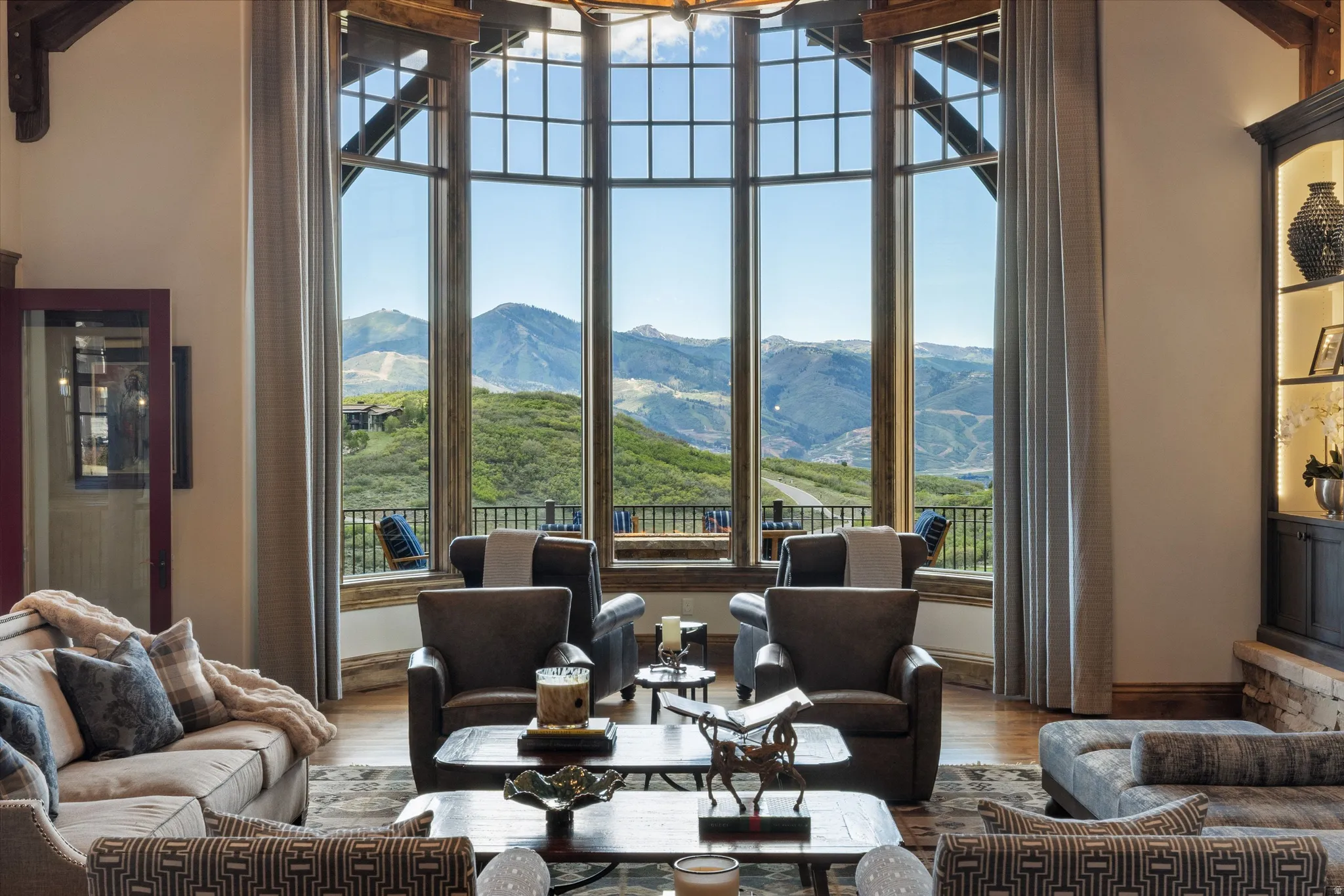 Vaulted ceiling living area featuring a large bay window with mountain scenery, exposed wood beams, and built-in shelving with accent lighting