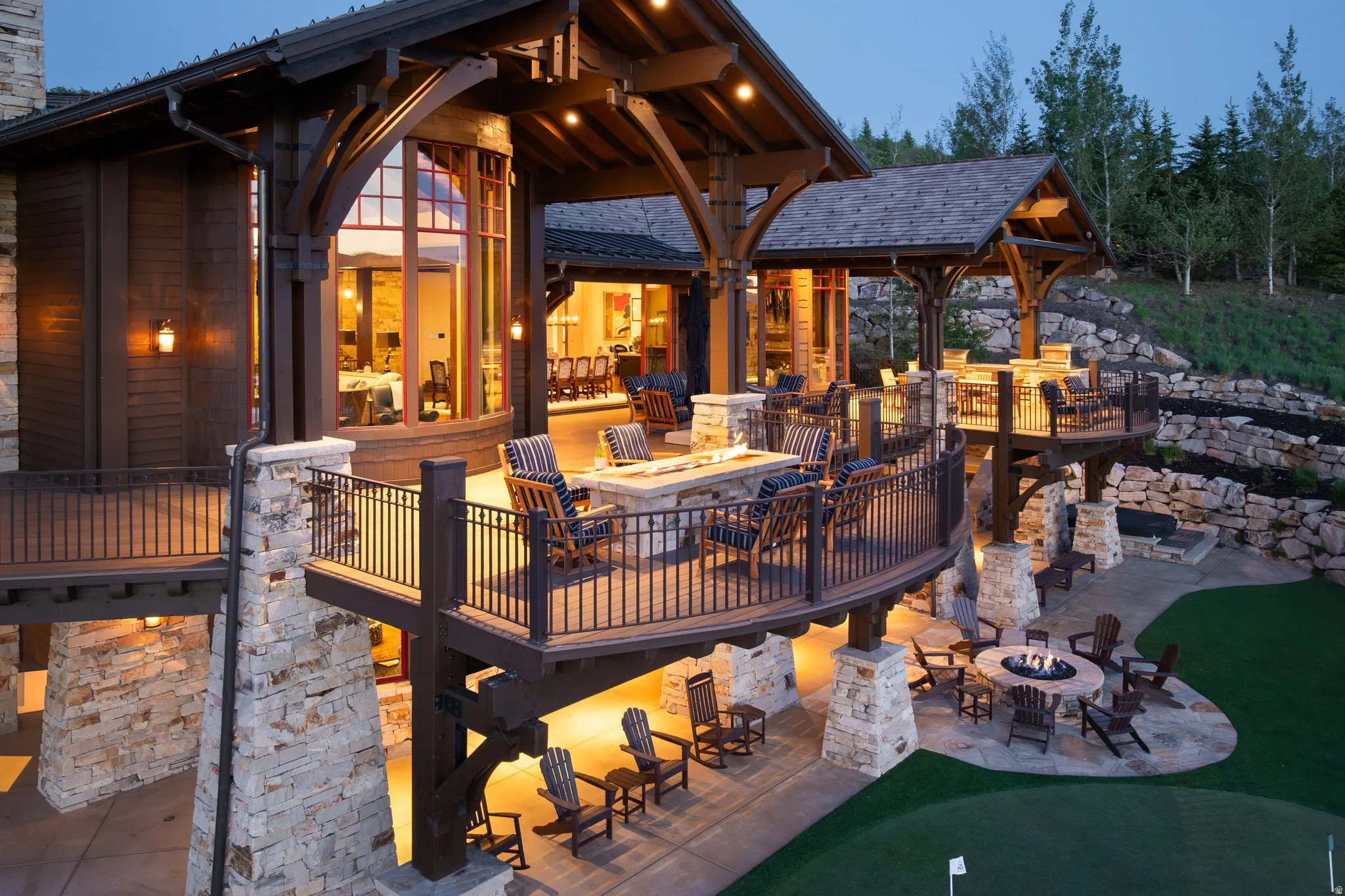 Multi-level outdoor living space featuring expansive decks, stone pillars, wrought iron railings, and exposed timber beams