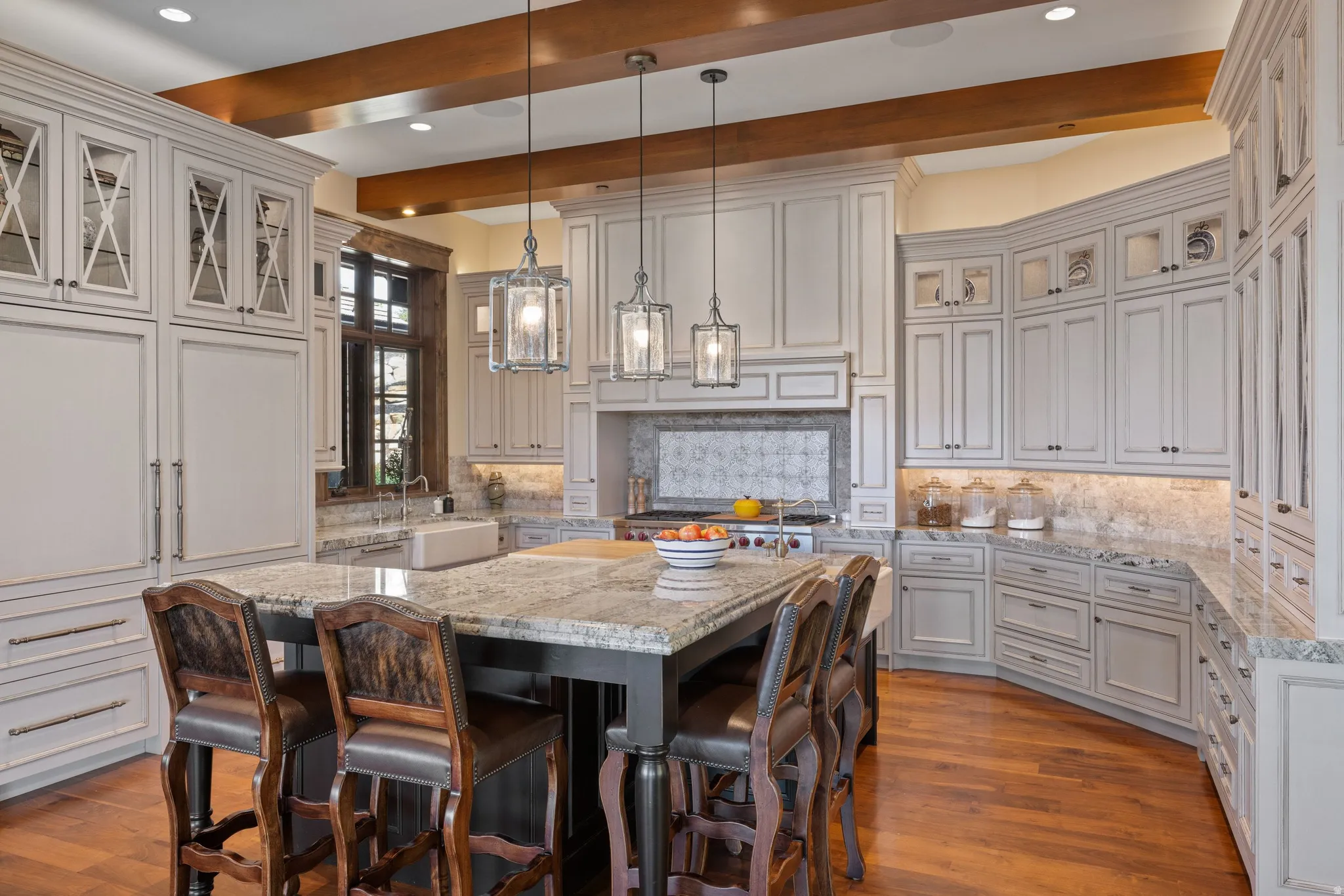 Gourmet kitchen featuring a large central island with seating, extensive custom cabinetry, granite countertops, wood-finish flooring, and exposed ceiling beams